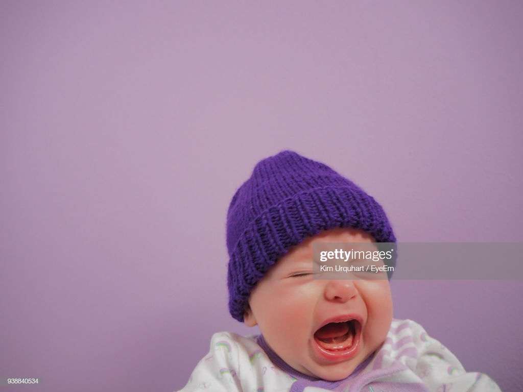 Closeup Of Crying Baby Against Purple Background High Res Stock