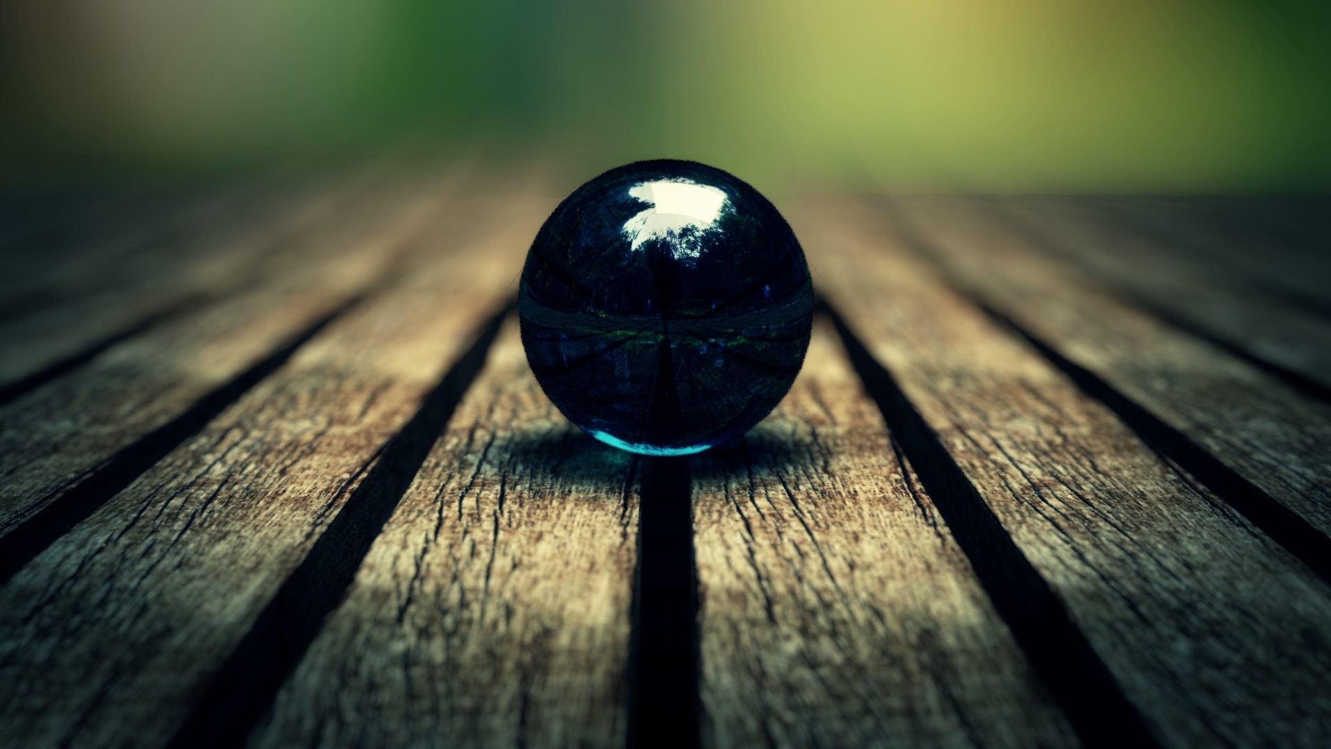 A dark blue glass marble rests on a weathered wooden surface, reflecting the blurred green background
