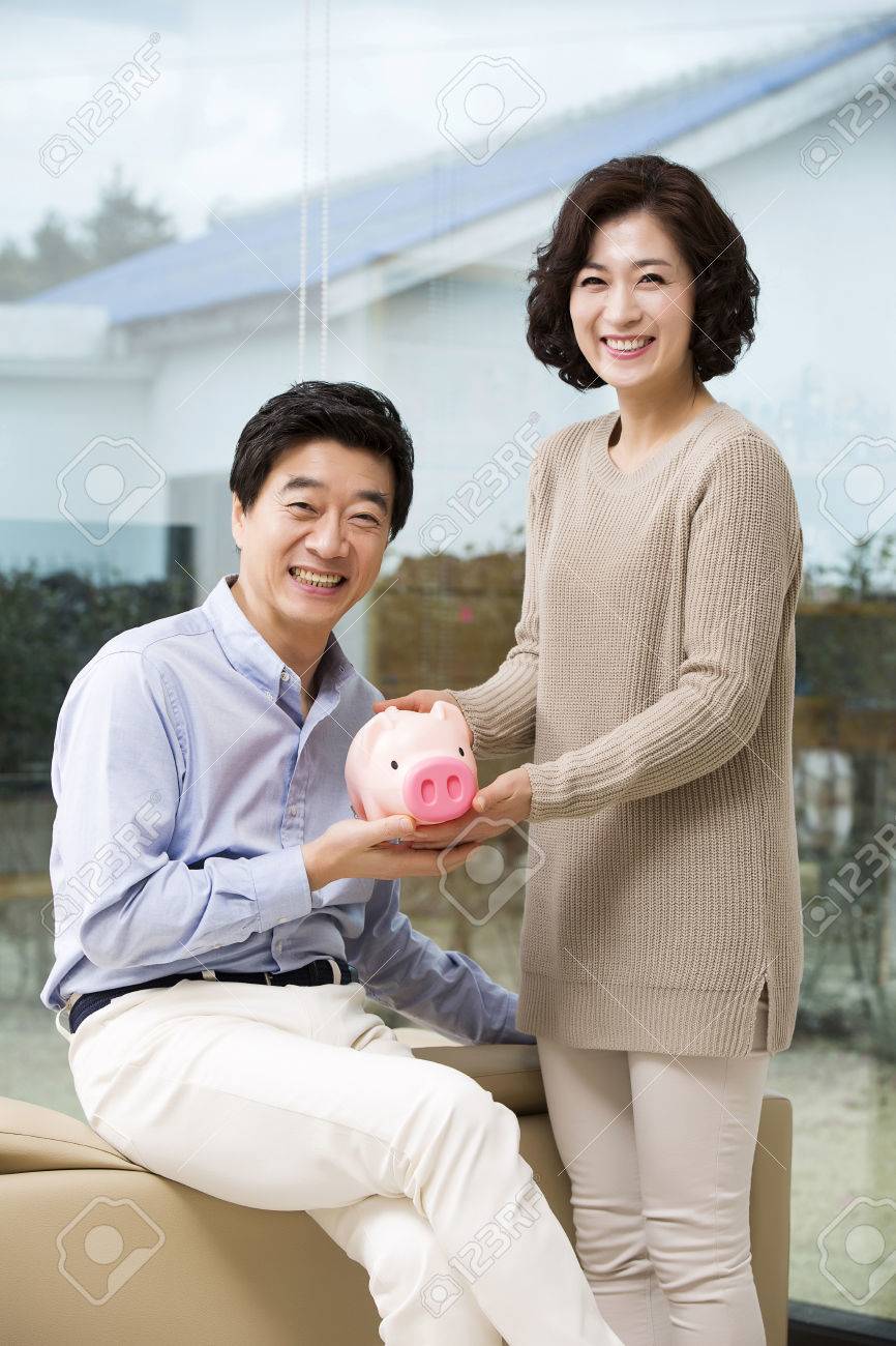 Happy Middleaged Asian Couple Holding A Piggy Bank Stock Photo