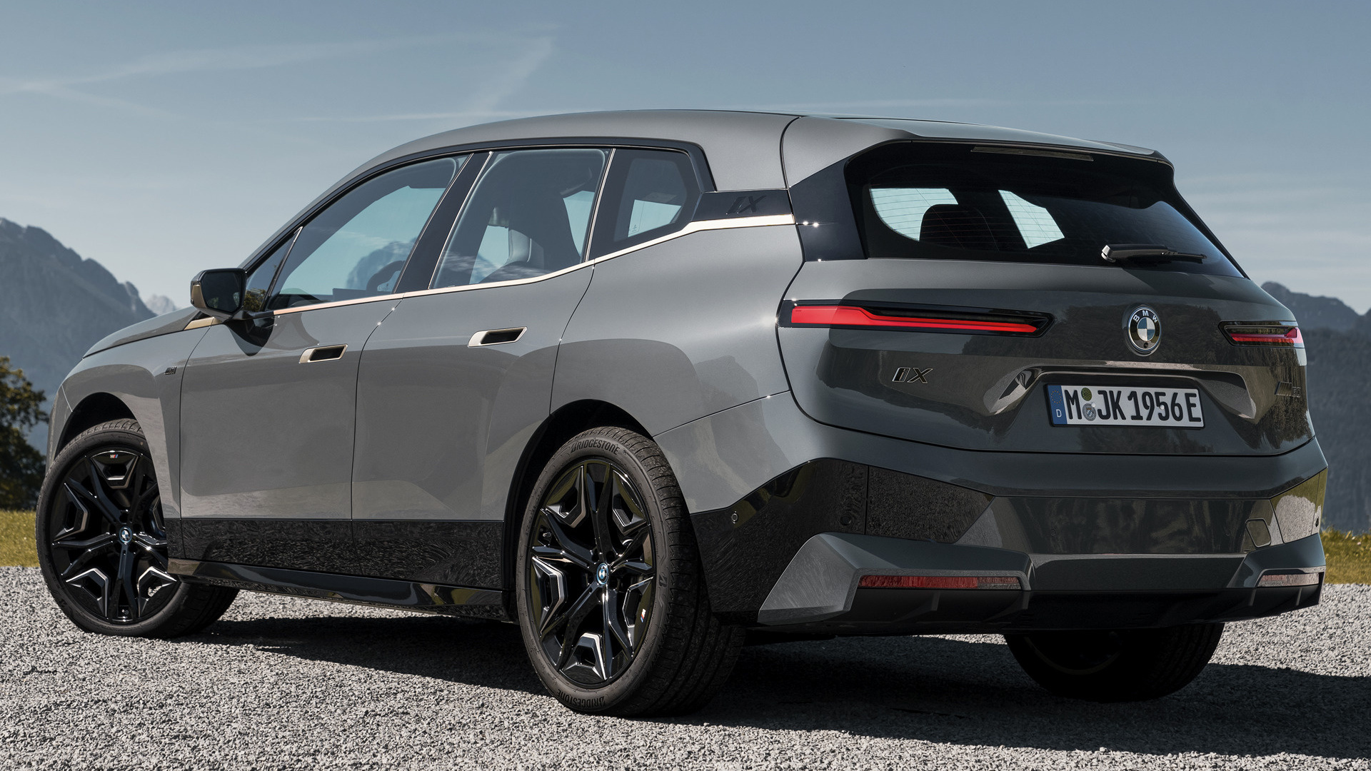 Rear view of a BMW iX electric SUV parked on a gravel road with mountains in the background