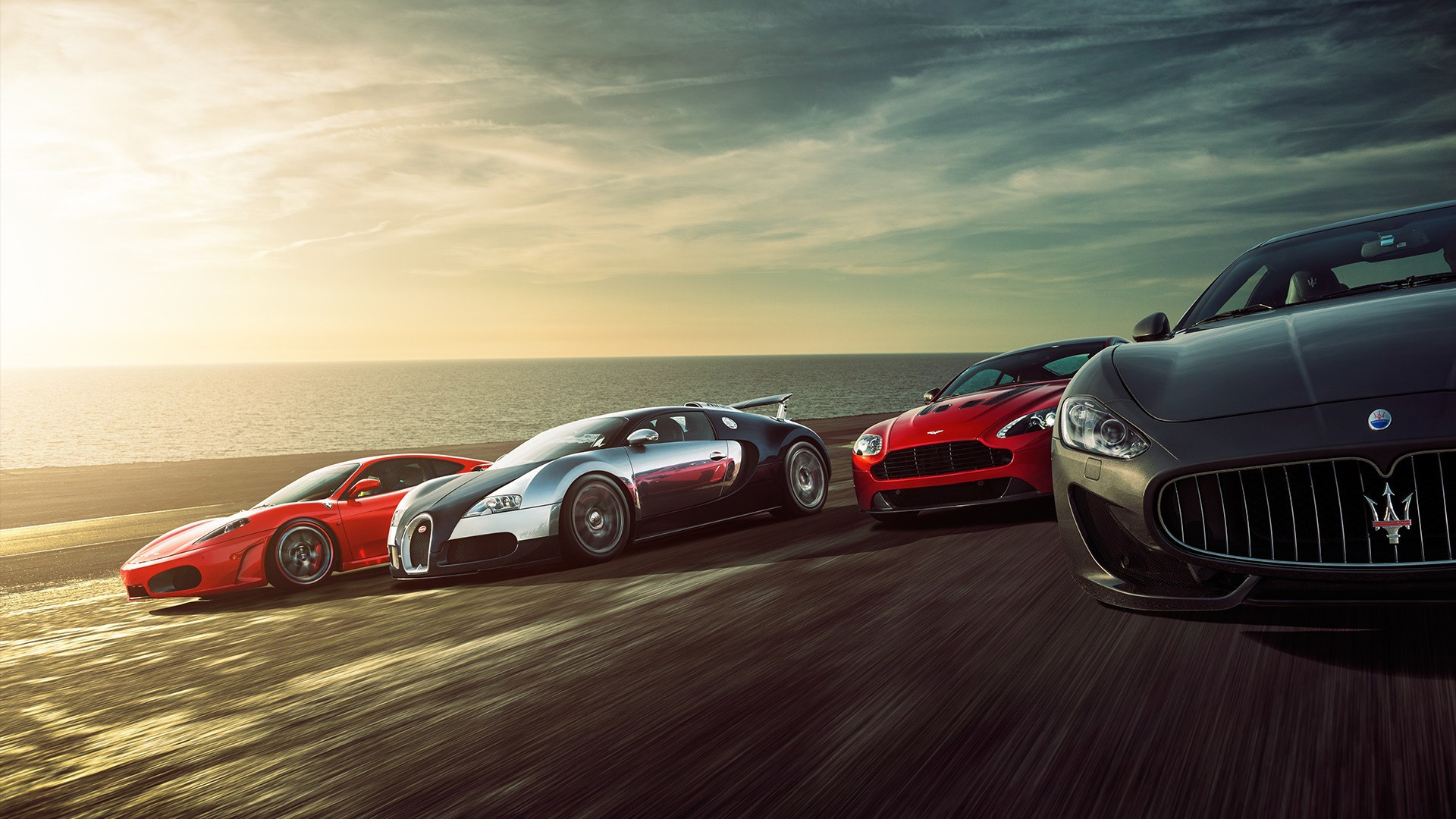 Four luxury sports cars speeding along a coastal road at sunset