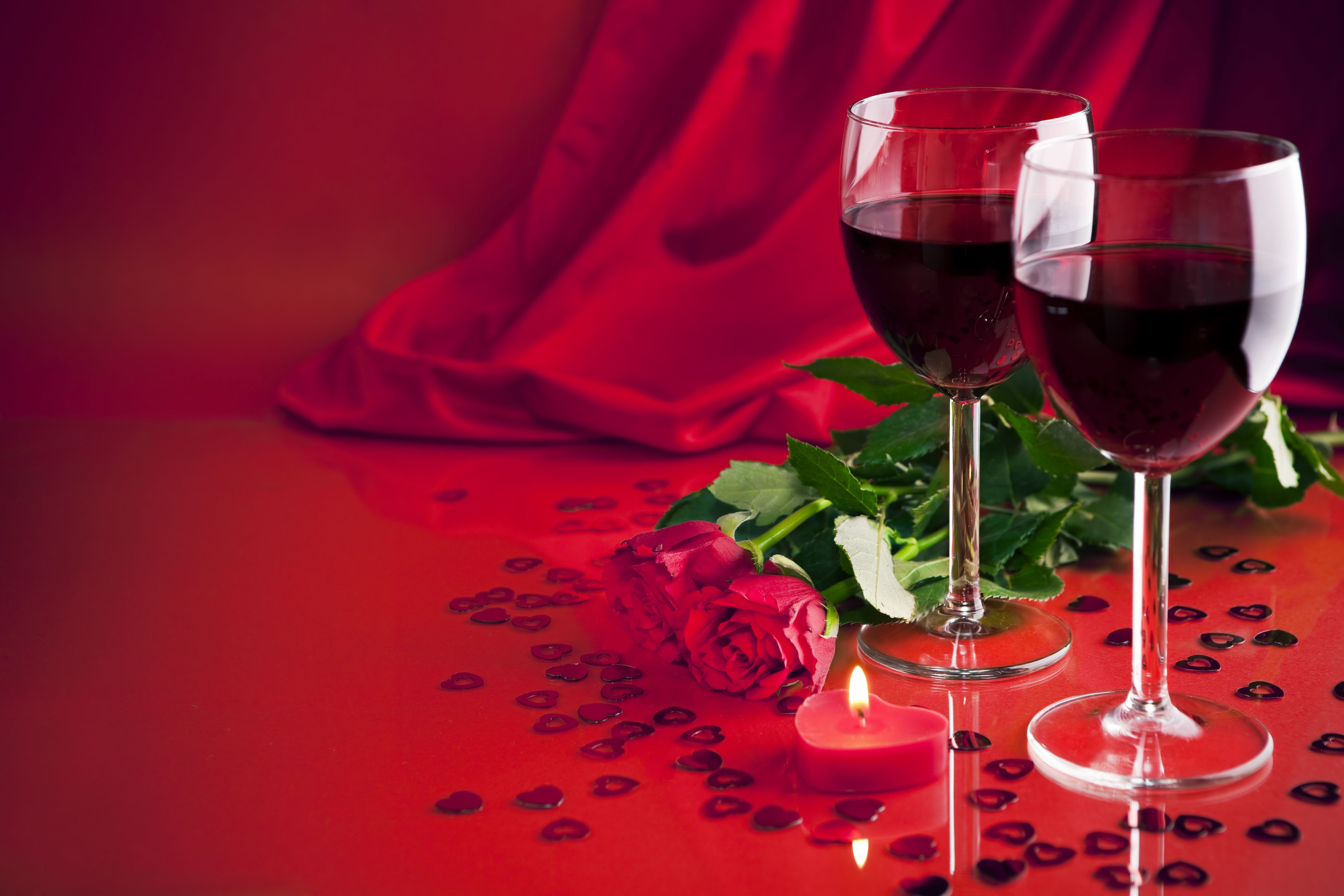 Romantic Valentine's Day setup with red wine, roses, and heart confetti