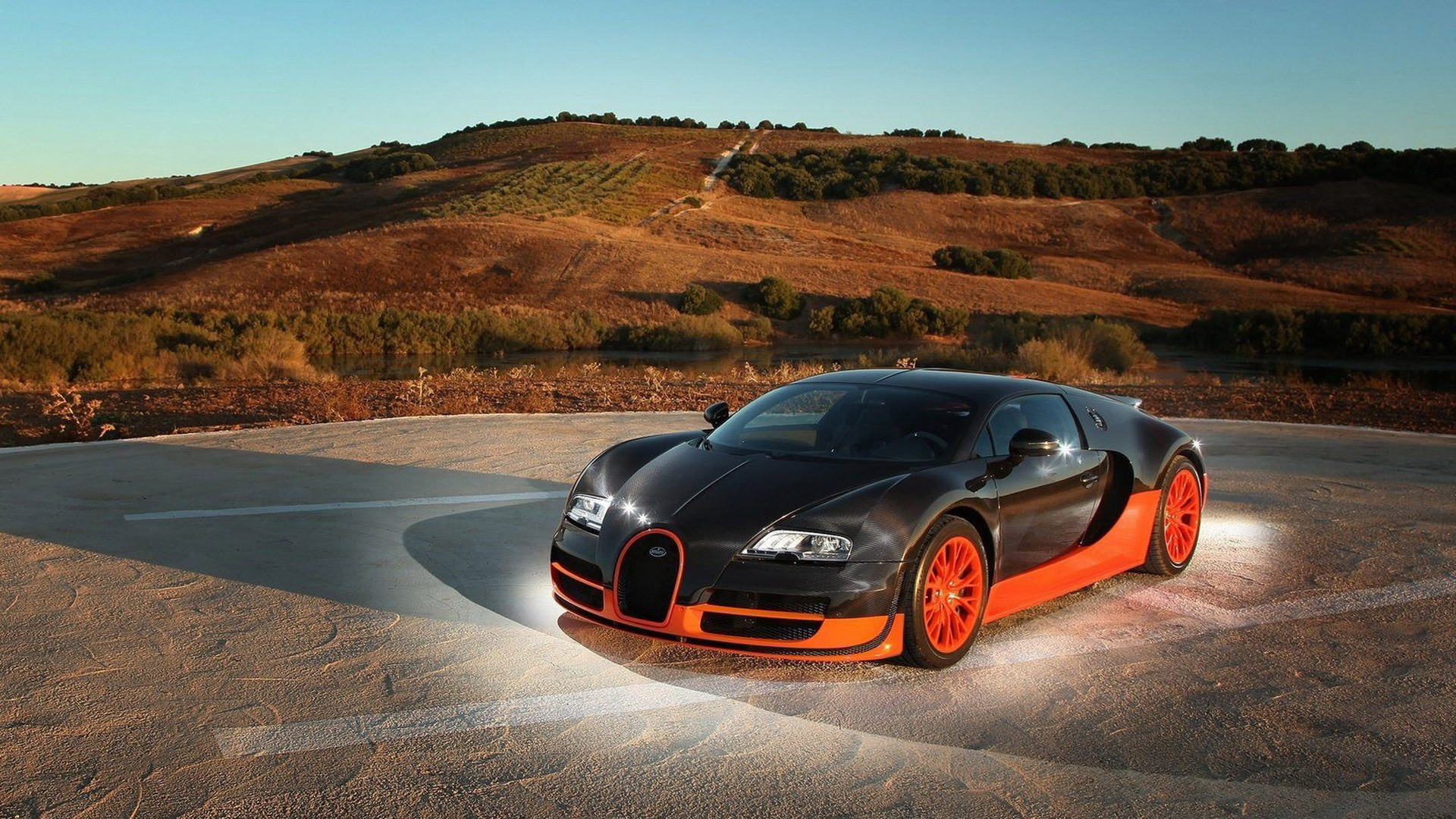 A black and orange Bugatti Veyron parked on a paved surface with a picturesque landscape in the background