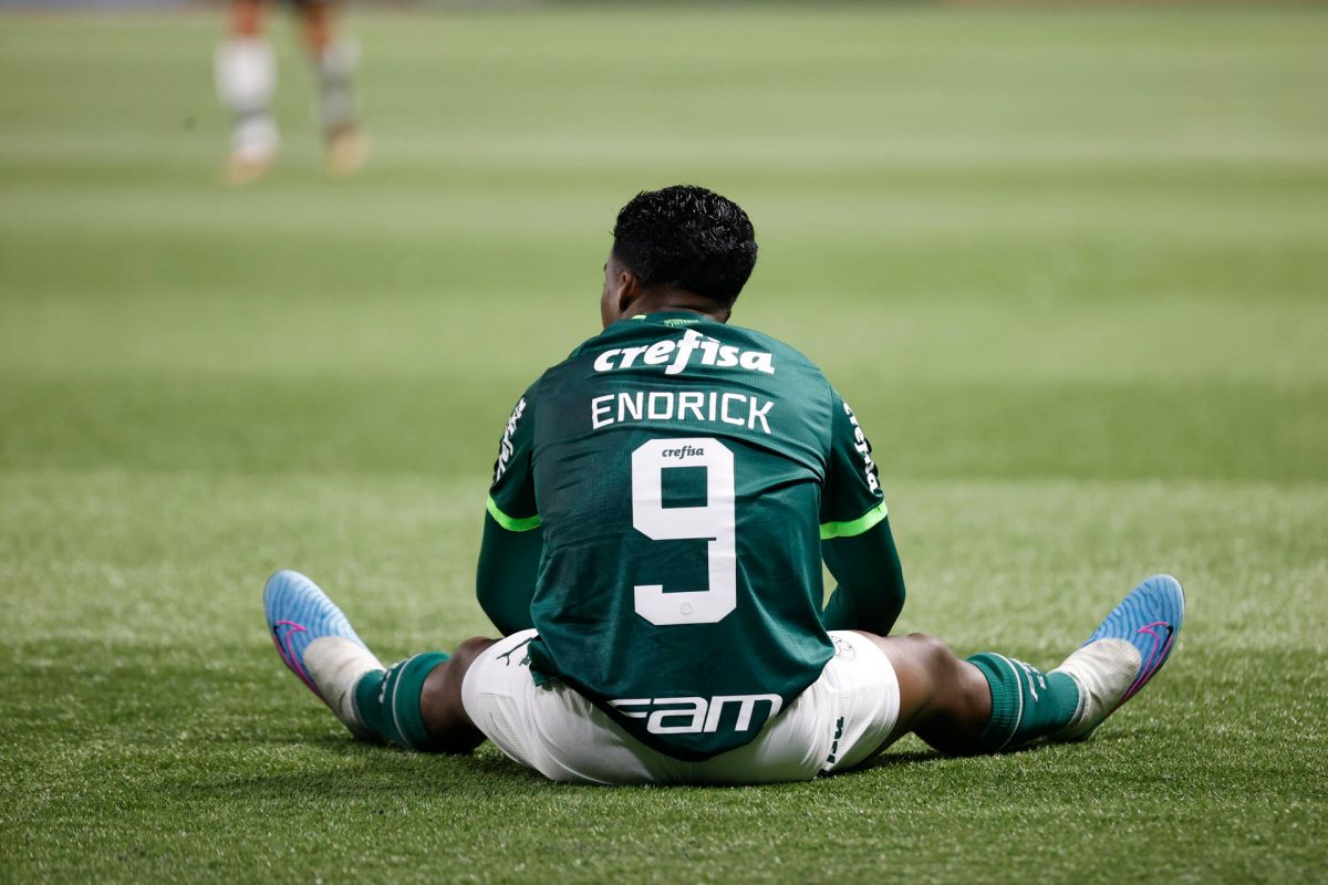 Endrick Felipe sits on the soccer field during a match, wearing his Palmeiras jersey with the number 9.  He appears to be taking a break or reflecting on the game