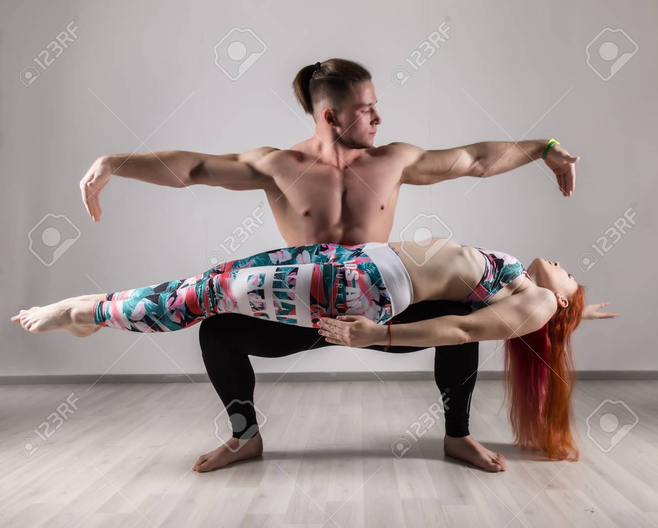 Sports Man And Woman Doing Acroyoga Exercises In A Gray Background