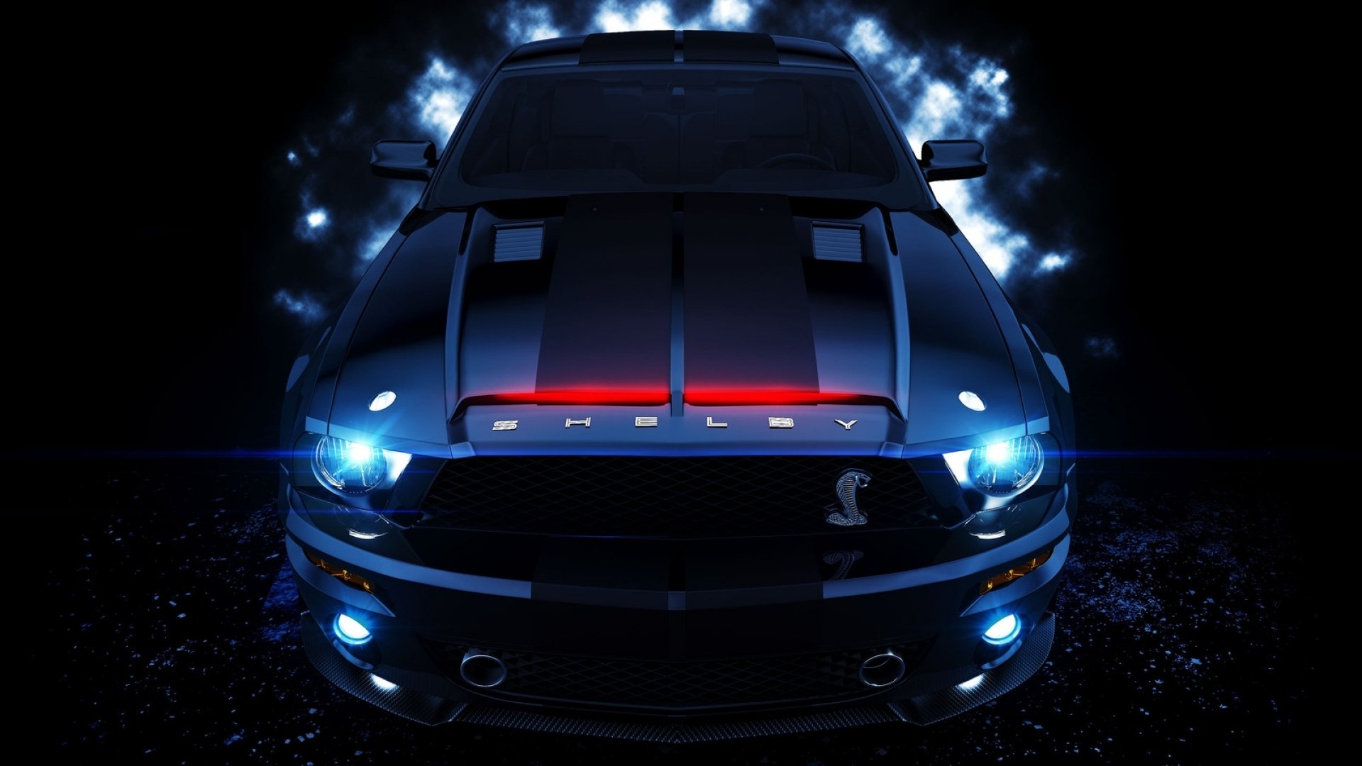 A front view of a dark blue Ford Mustang Shelby GT500 at night, illuminated by its bright headlights and a red light bar above the grille. The car's hood features racing stripes and air intakes, adding to its aggressive and powerful look
