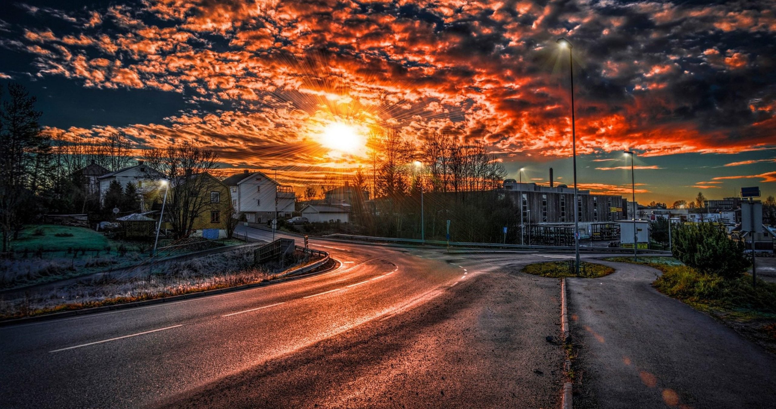 A breathtaking 4k wallpaper featuring a vibrant sunset over a winding road, casting a warm glow on the surrounding houses and trees