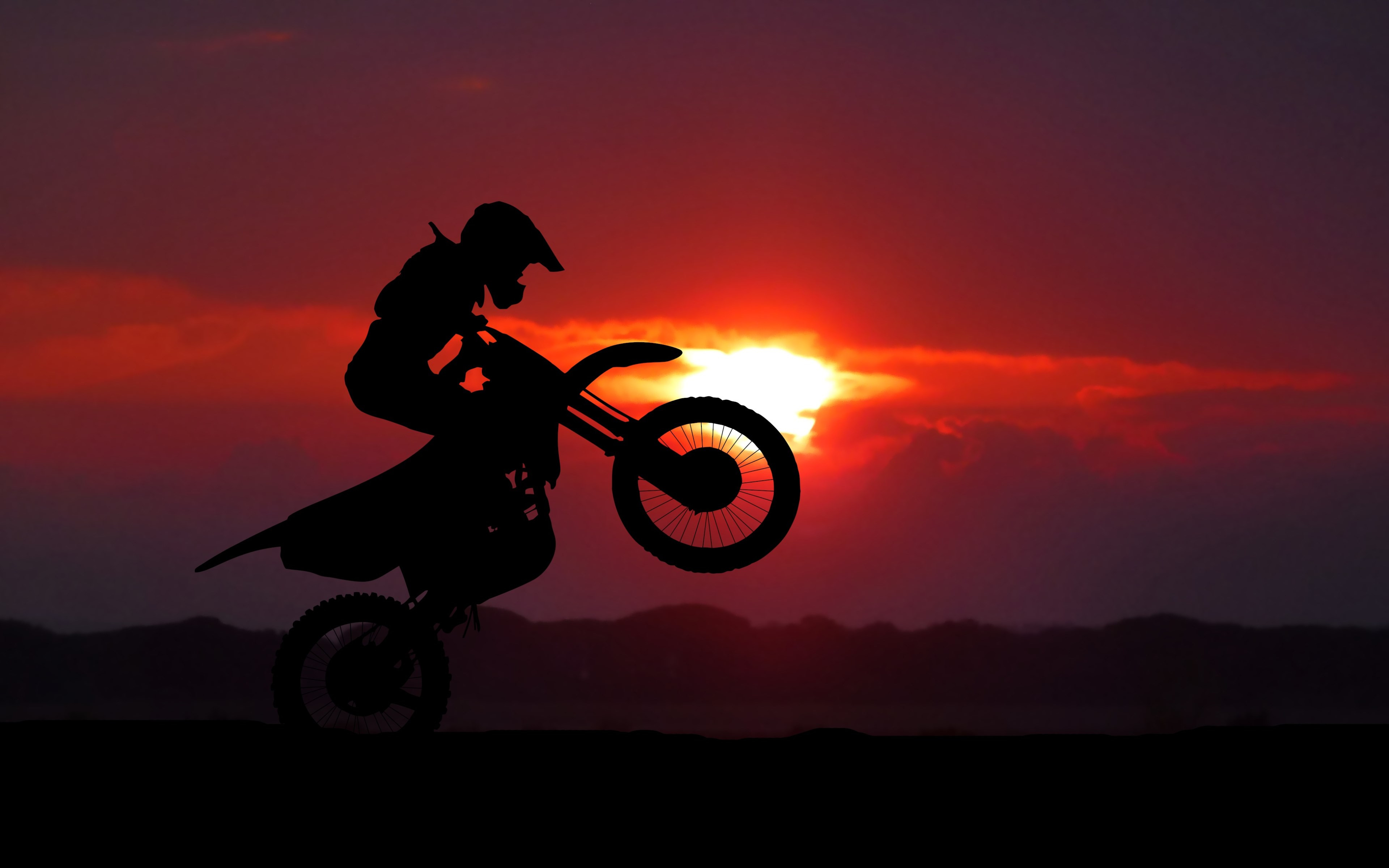 Silhouette of a motocross rider performing a wheelie against a vibrant sunset backdrop