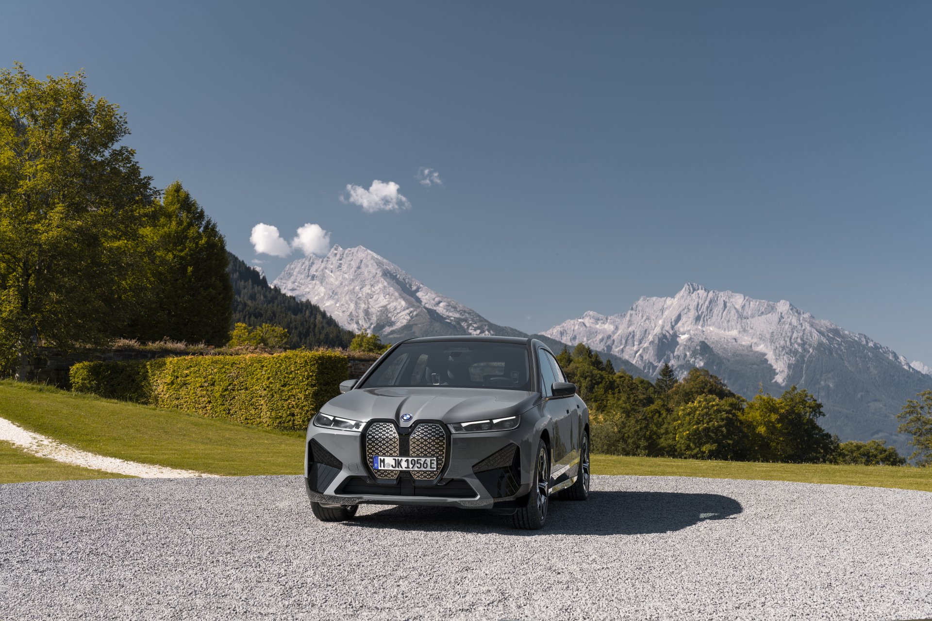 A sleek, gray BMW iX electric SUV parked majestically against a breathtaking backdrop of snow-capped Alpine mountains