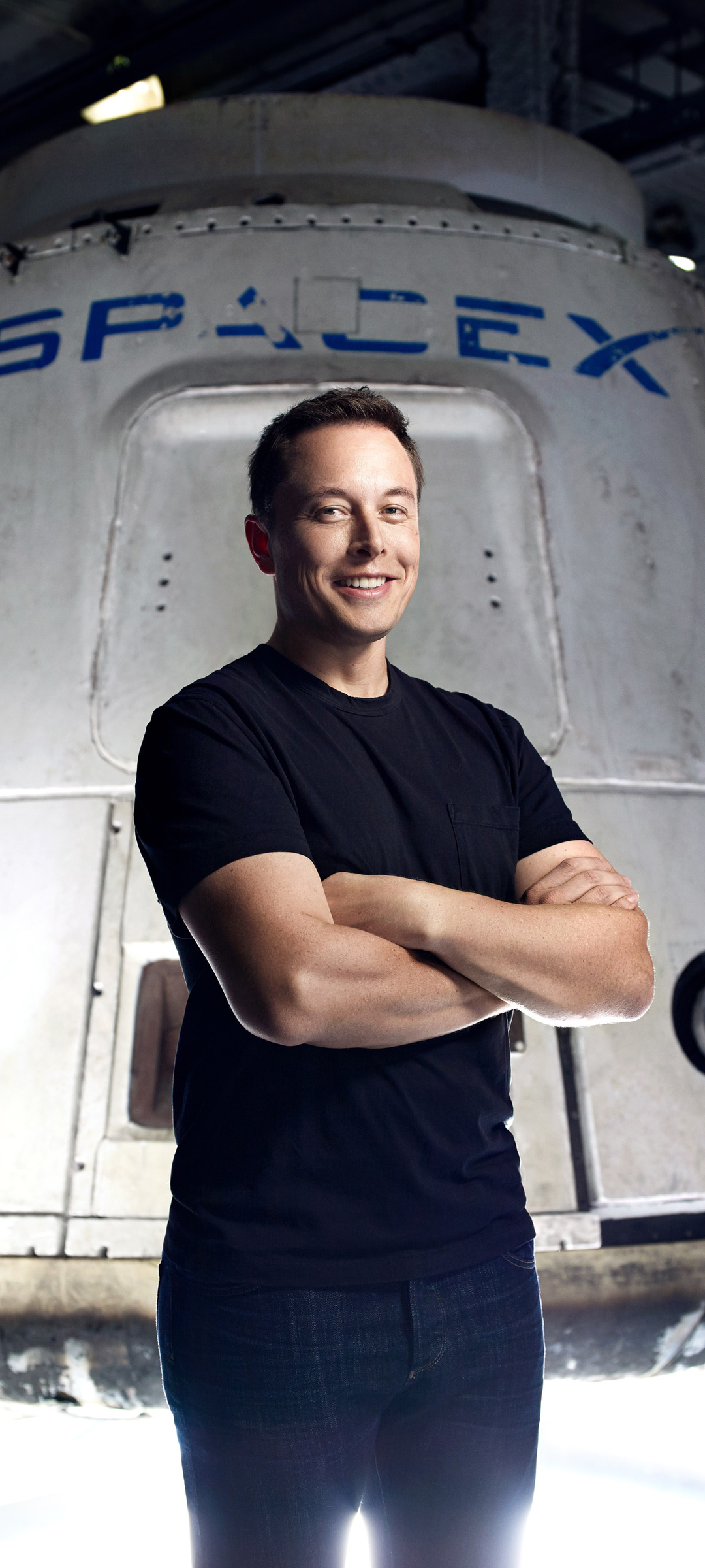 Elon Musk, CEO of SpaceX, stands proudly in front of a SpaceX Crew Dragon spacecraft with his arms crossed, smiling confidently