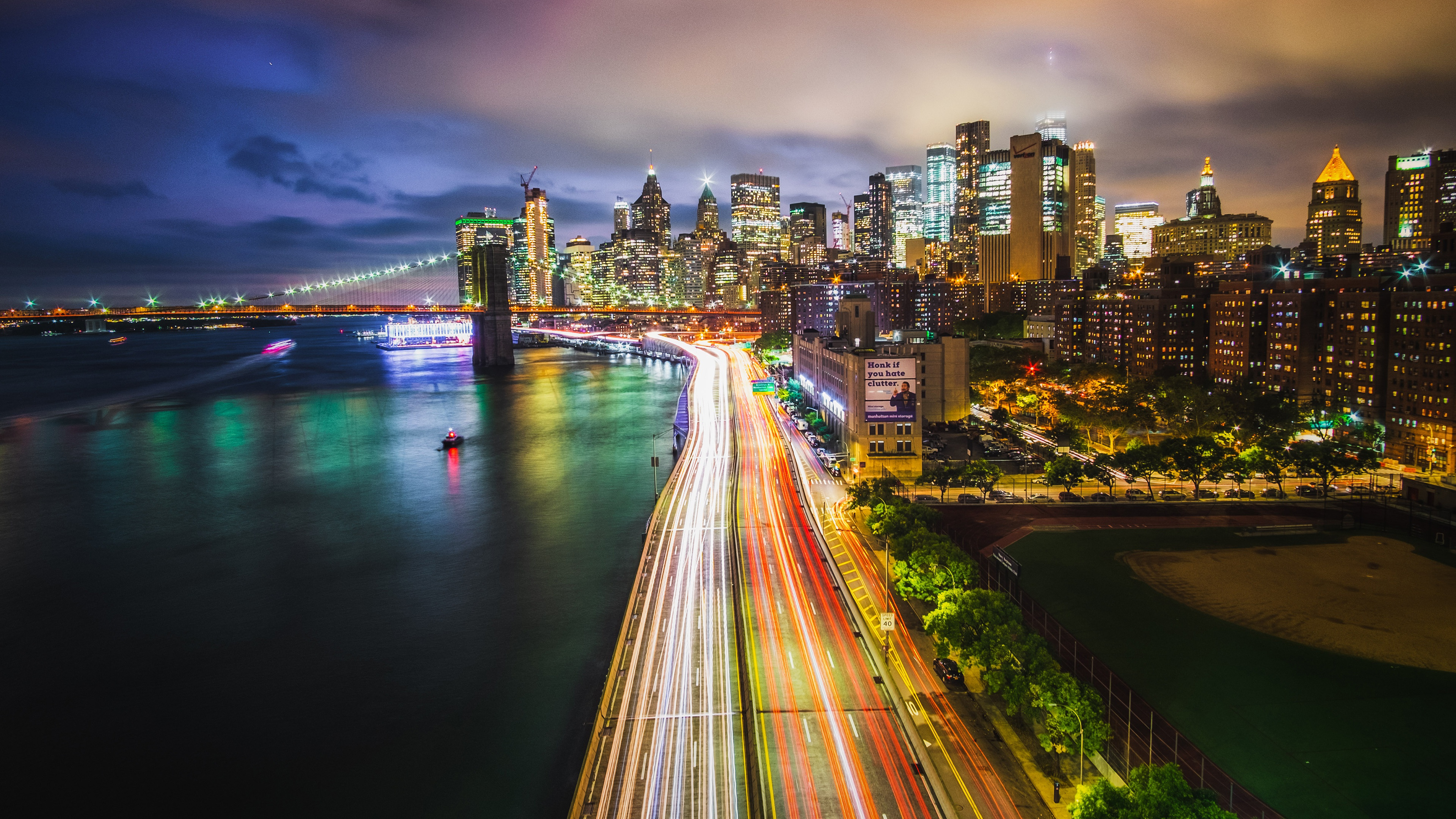 A stunning 4K wallpaper of New York City at night, featuring the Brooklyn Bridge, illuminated skyscrapers, and the FDR Drive light trails