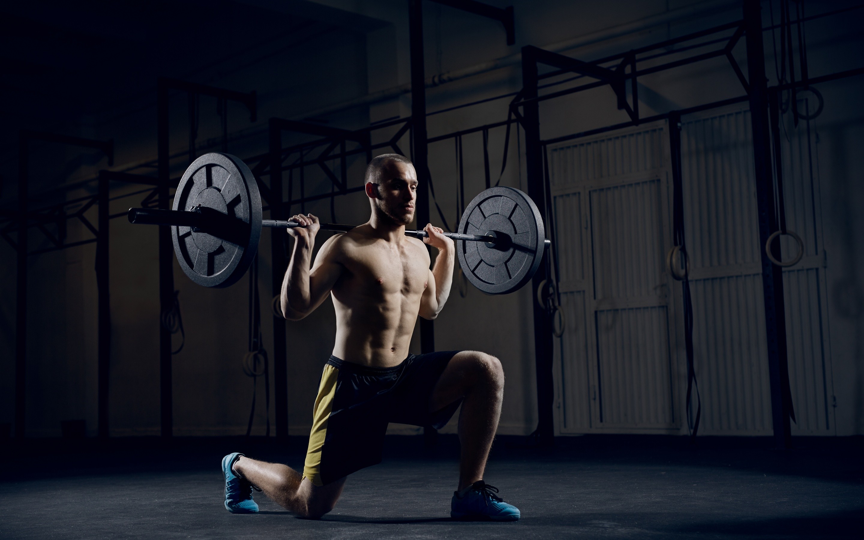 A muscular man performing a barbell lunge in a CrossFit gym, demonstrating strength and athleticism
