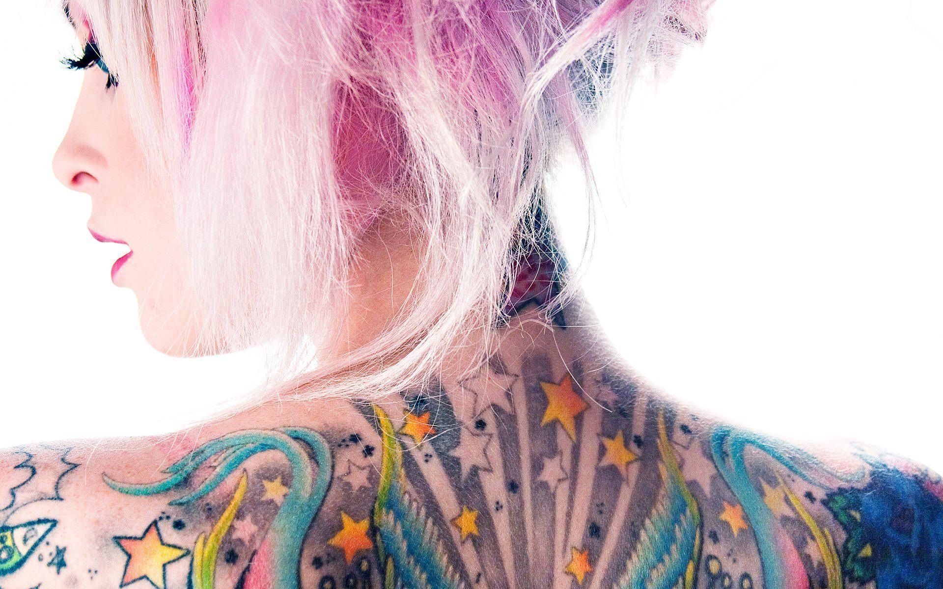 Woman with colorful tattoos on her back and shoulders, showcasing a variety of designs and bright colors against pale skin