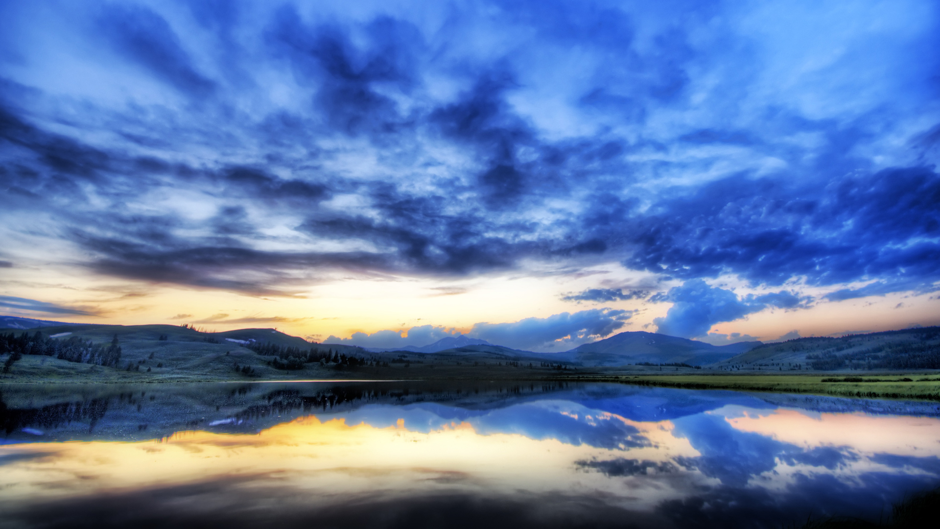 A breathtaking sunset reflected in a calm lake, with rolling hills and a vibrant sky