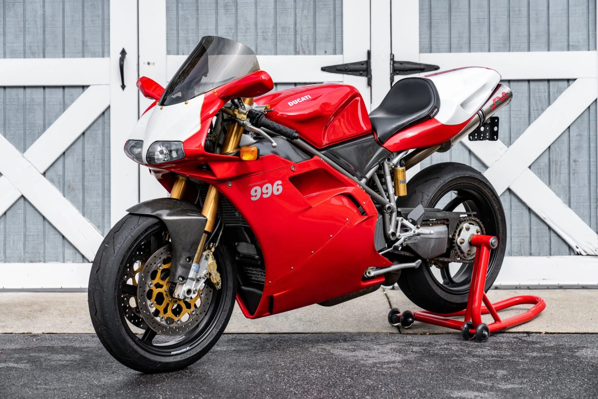Ducati 996 sportbike in red and white, parked in front of a gray barn door