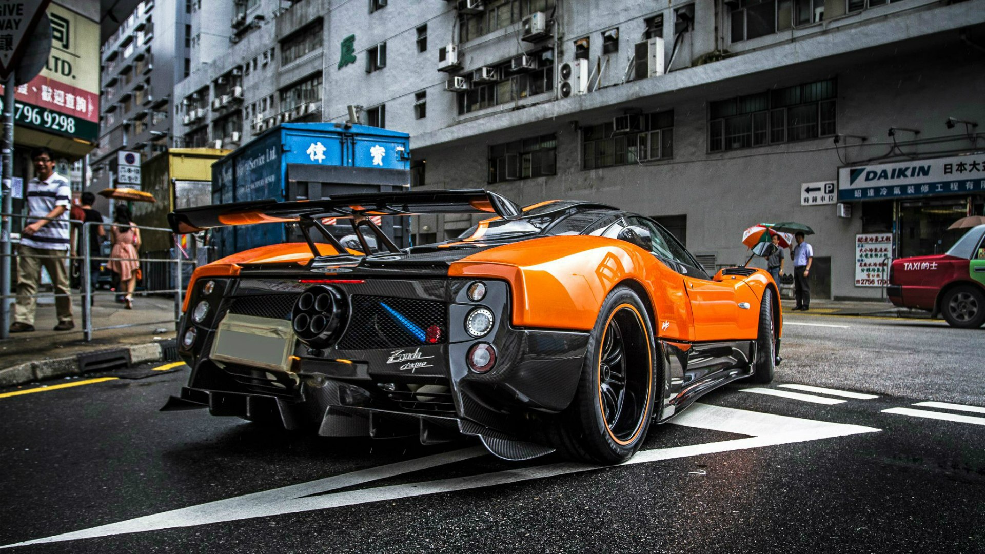 A vibrant orange and black Pagani Zonda sports car parked on a city street