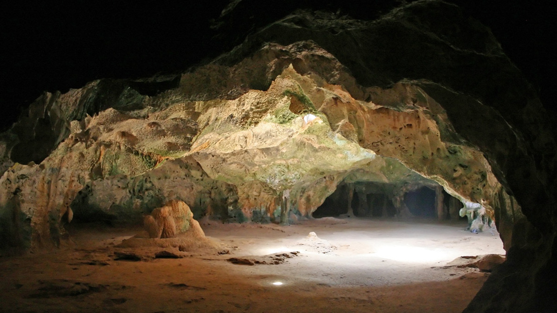 A mesmerizing view inside a dimly lit cave, showcasing intricate rock formations and a sandy floor