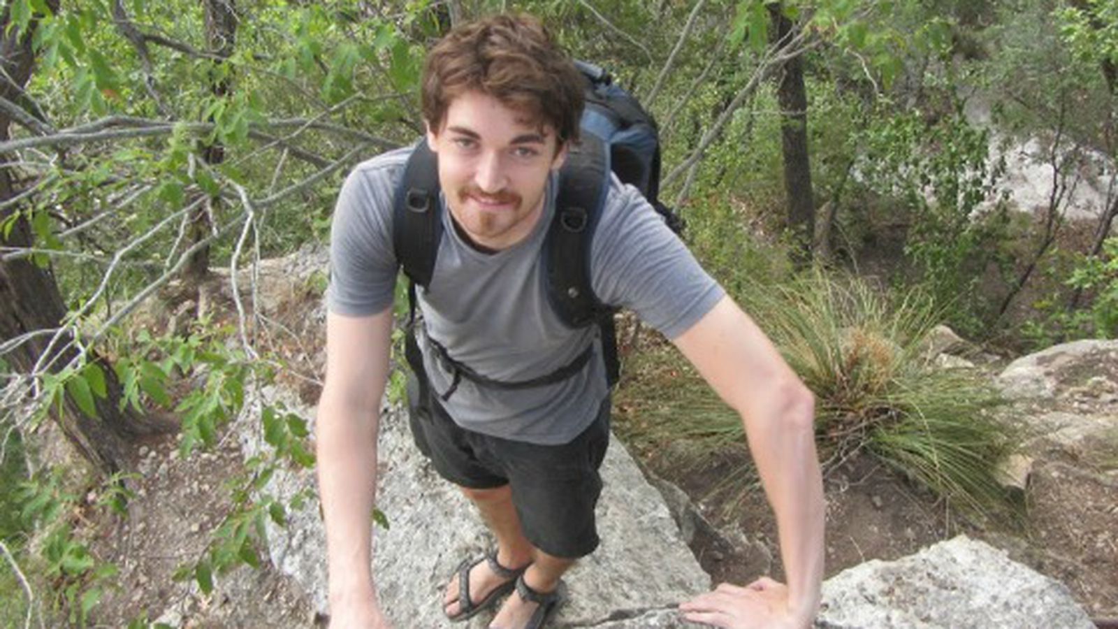 A man with brown hair and a gray shirt hiking on a rocky terrain