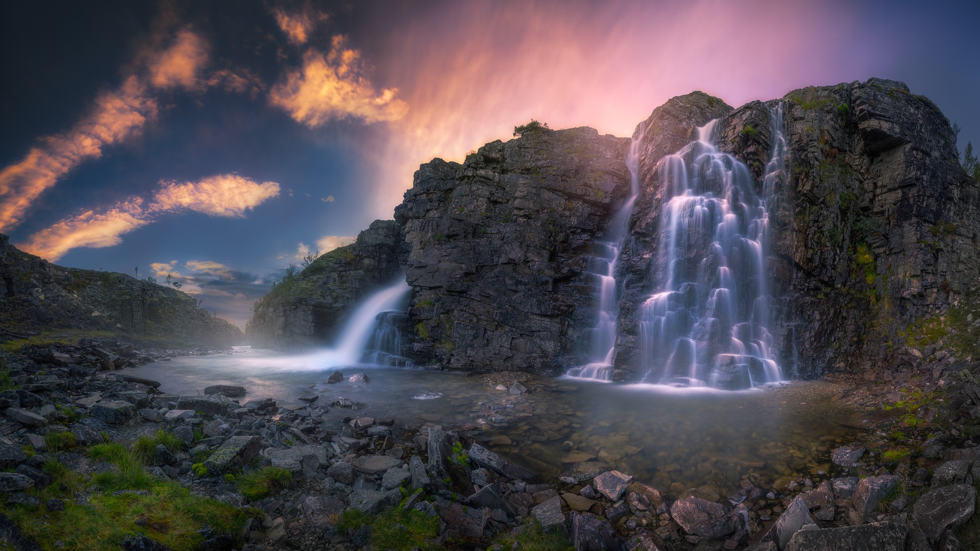 A breathtaking waterfall cascades down a rocky cliff face under a vibrant sunset sky in this stunning 1920x1080 wallpaper
