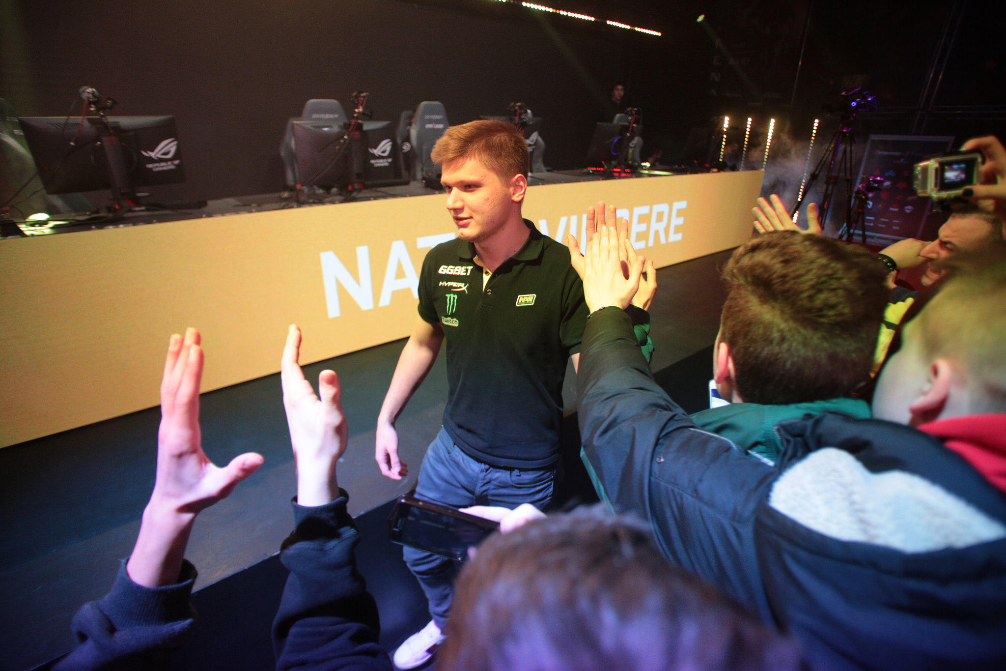 A man in a black polo shirt with green accents high-fives fans in a crowd