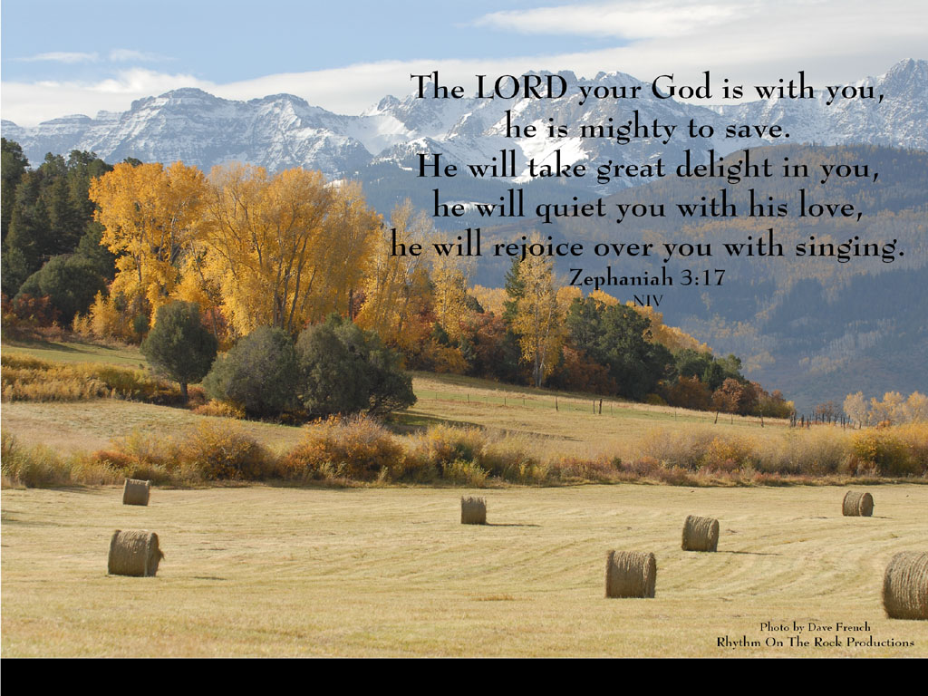 A scenic autumn landscape with hay bales in the foreground and snow-capped mountains in the background, accompanied by the Bible verse Zephaniah 3:17
