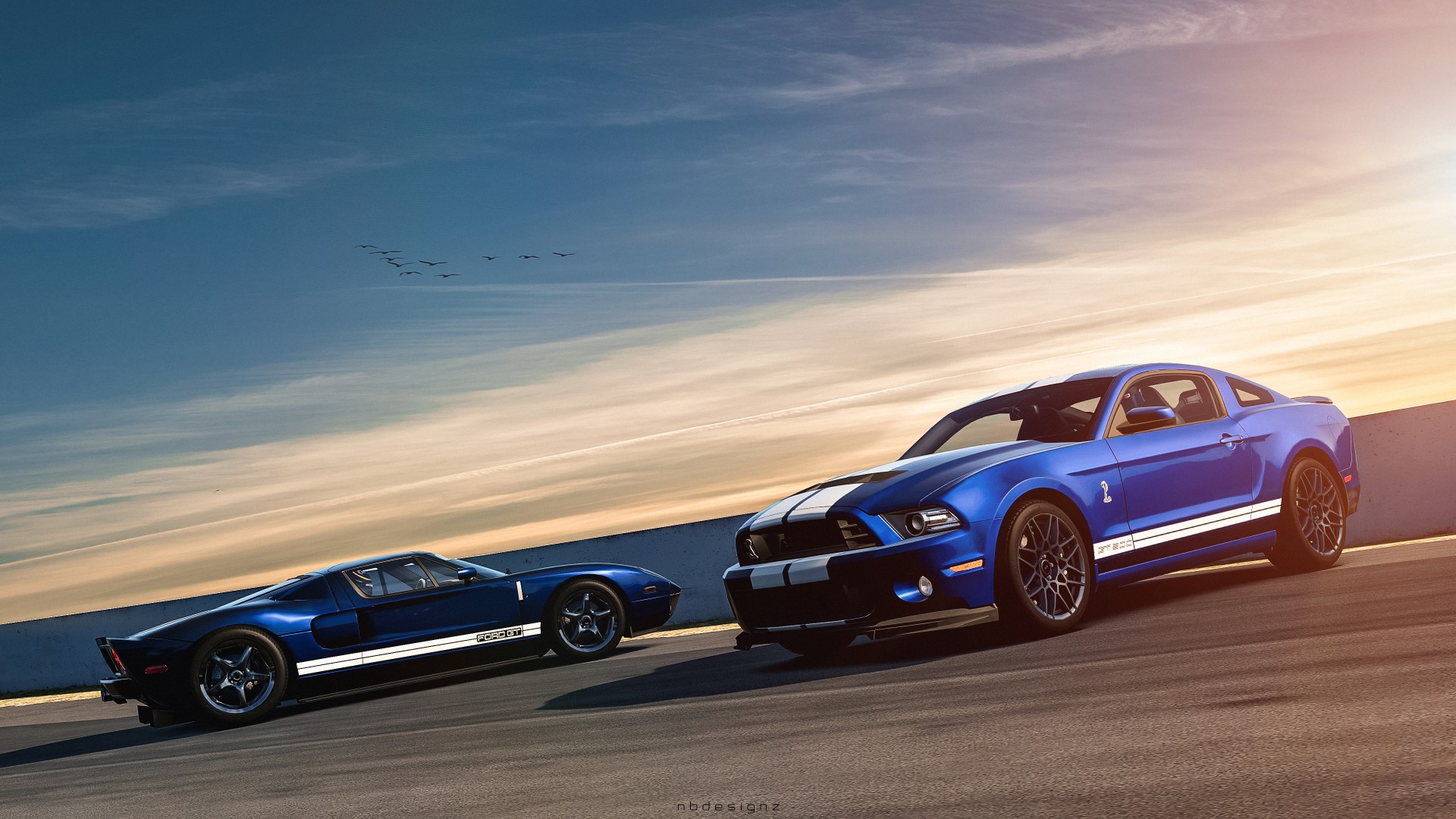 Two blue Ford Mustangs, a classic and a modern Shelby GT500, parked on a race track under a sunset sky