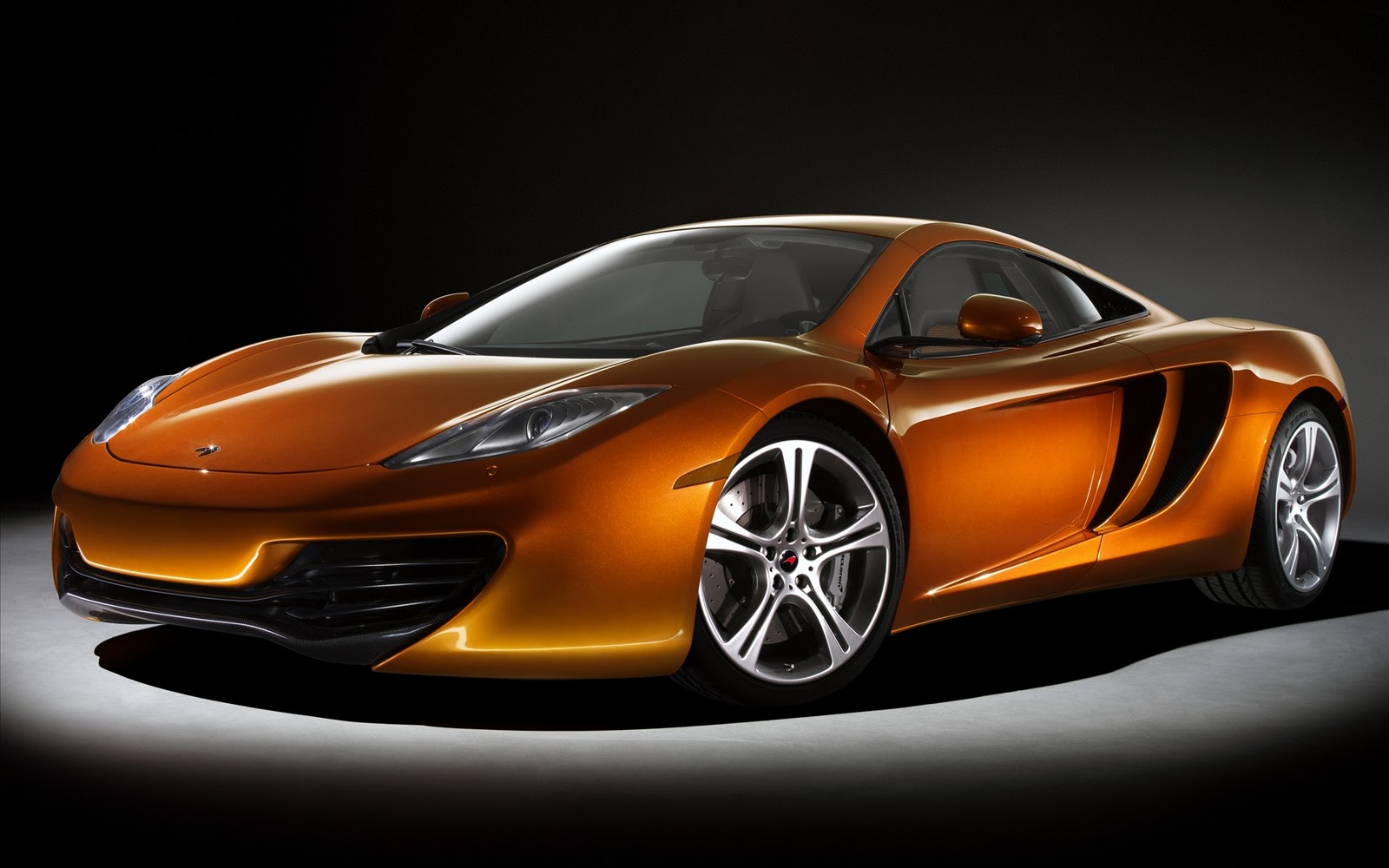 A sleek, orange McLaren MP4-12C sports car against a dark background
