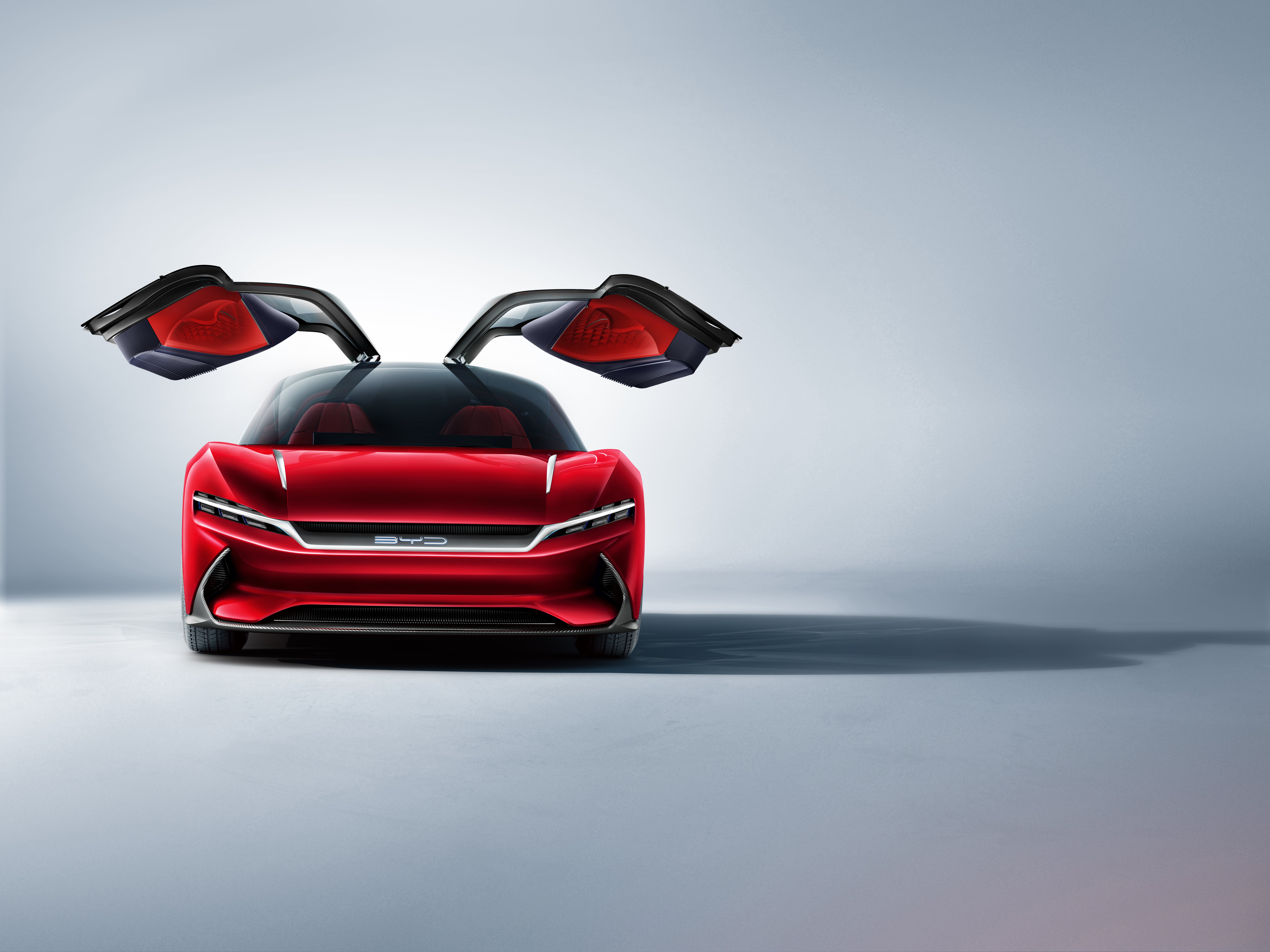 A red BYD electric sports car with its futuristic butterfly doors open, showcasing a sleek and modern design against a minimalist background