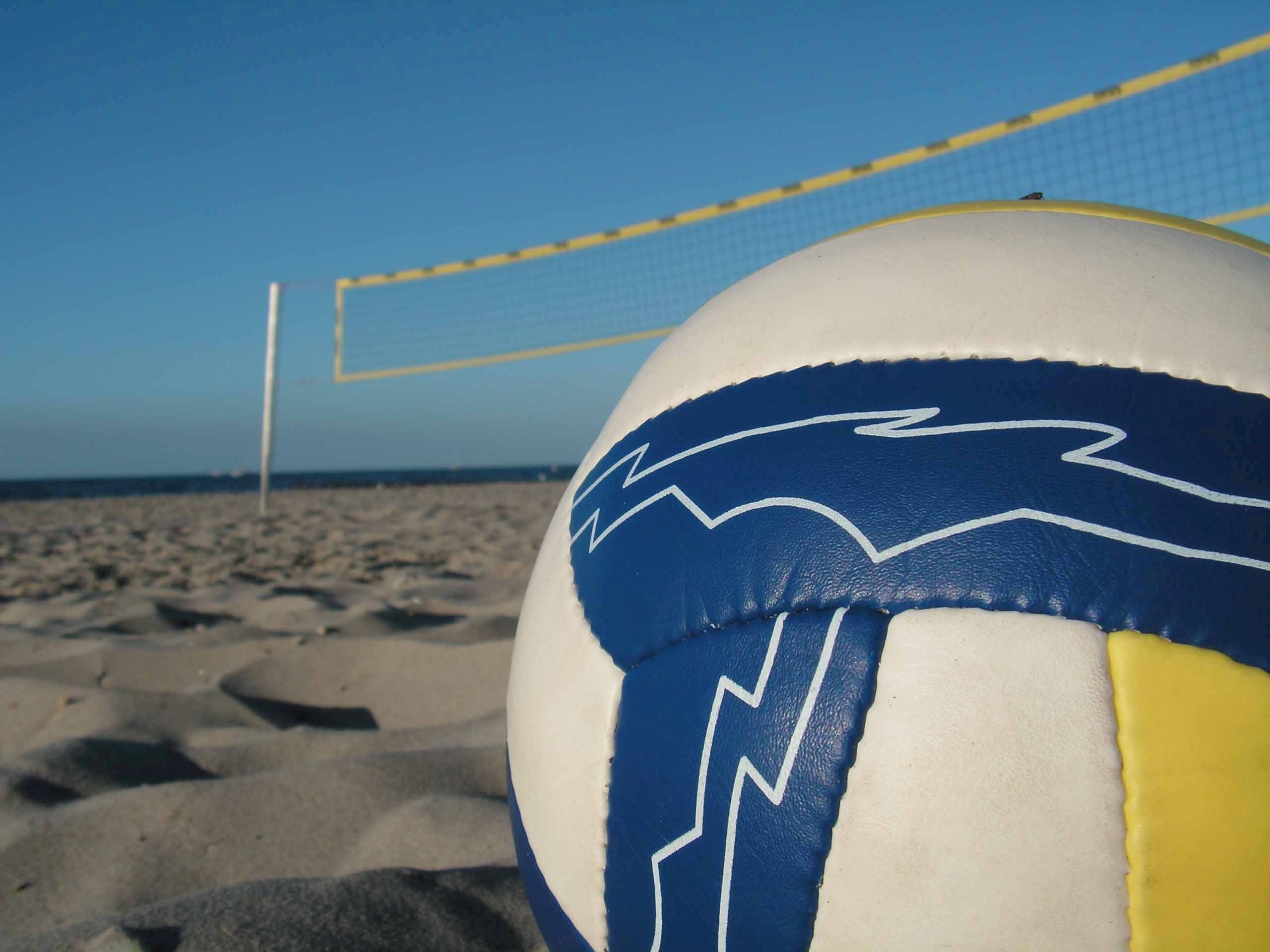 A close-up of a beach volleyball on the sand with a net and the ocean in the background