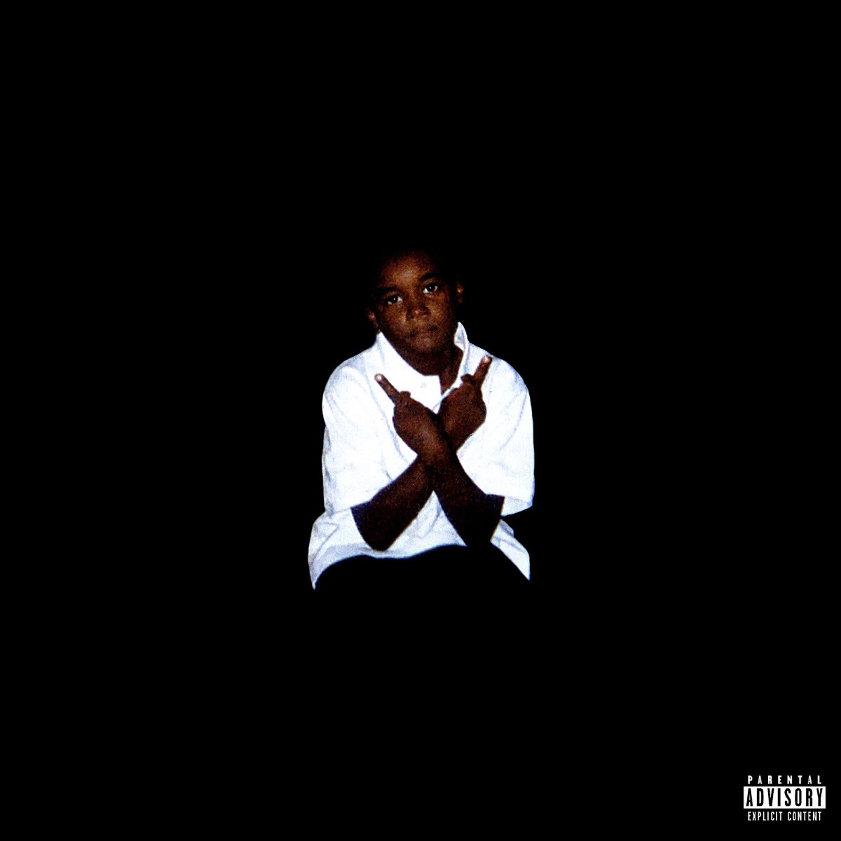 A young boy wearing a white shirt, against a black background, makes a hand gesture
