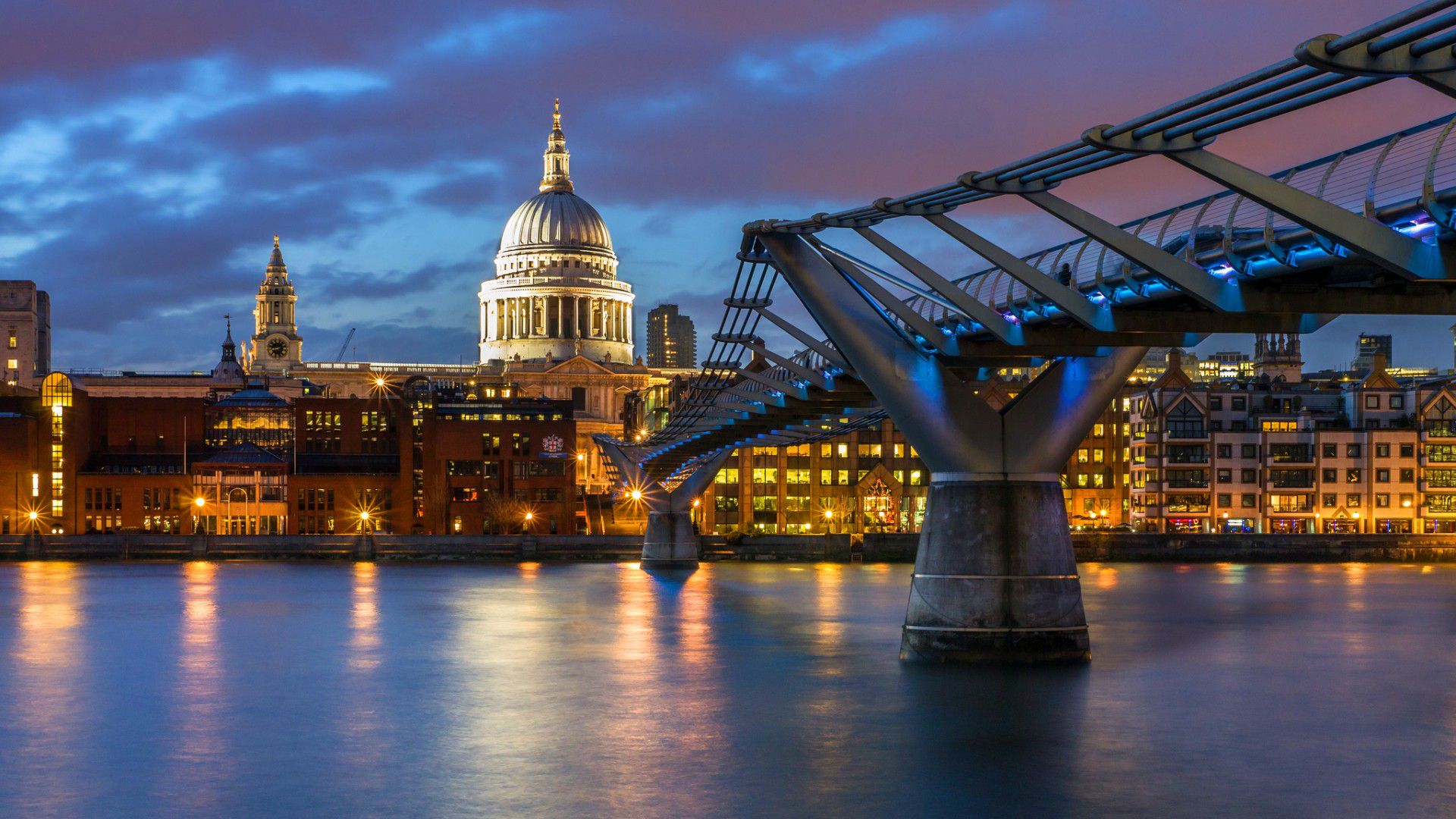 A stunning night view of St. Paul's Cathedral and the Millennium Bridge in London, UK, with the city lights reflecting on the Thames River