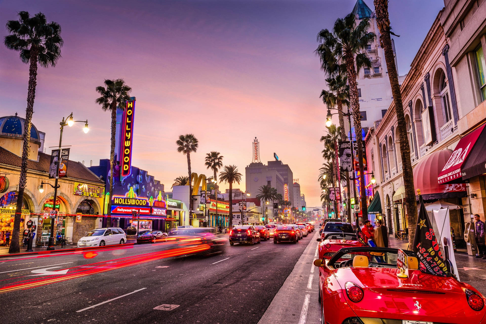 A vibrant sunset over Hollywood Boulevard, showcasing the iconic Hollywood sign, palm trees, and bustling city life