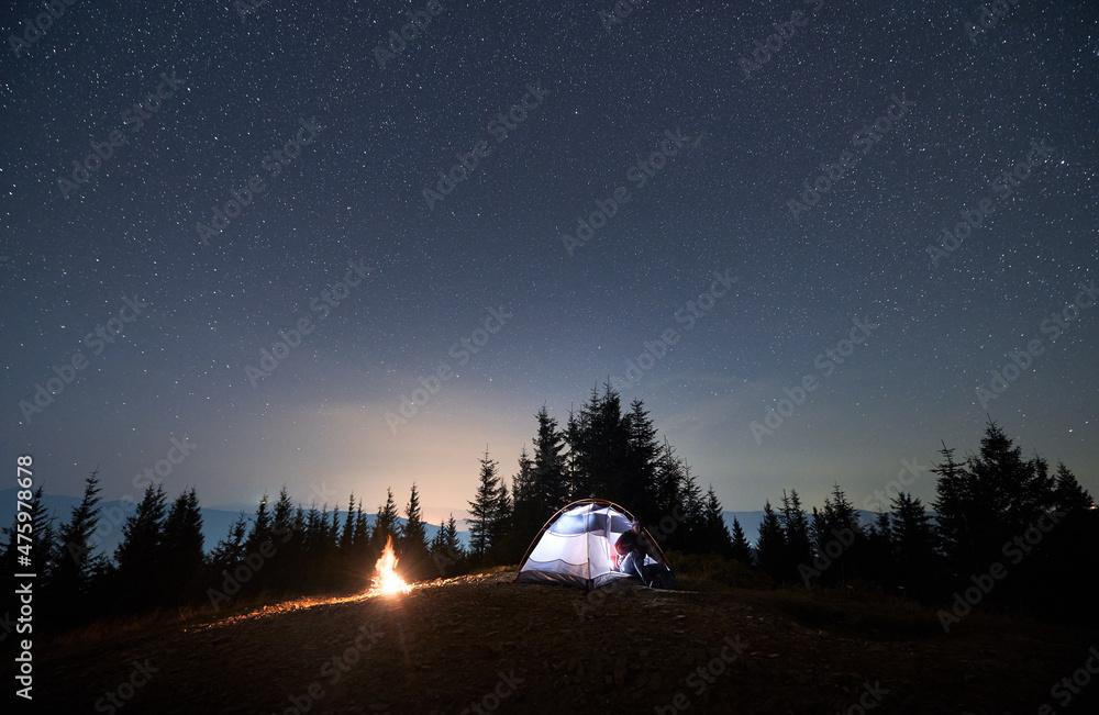 Tourist Man Sitting In His Illuminated Tent Set Up On Mountain