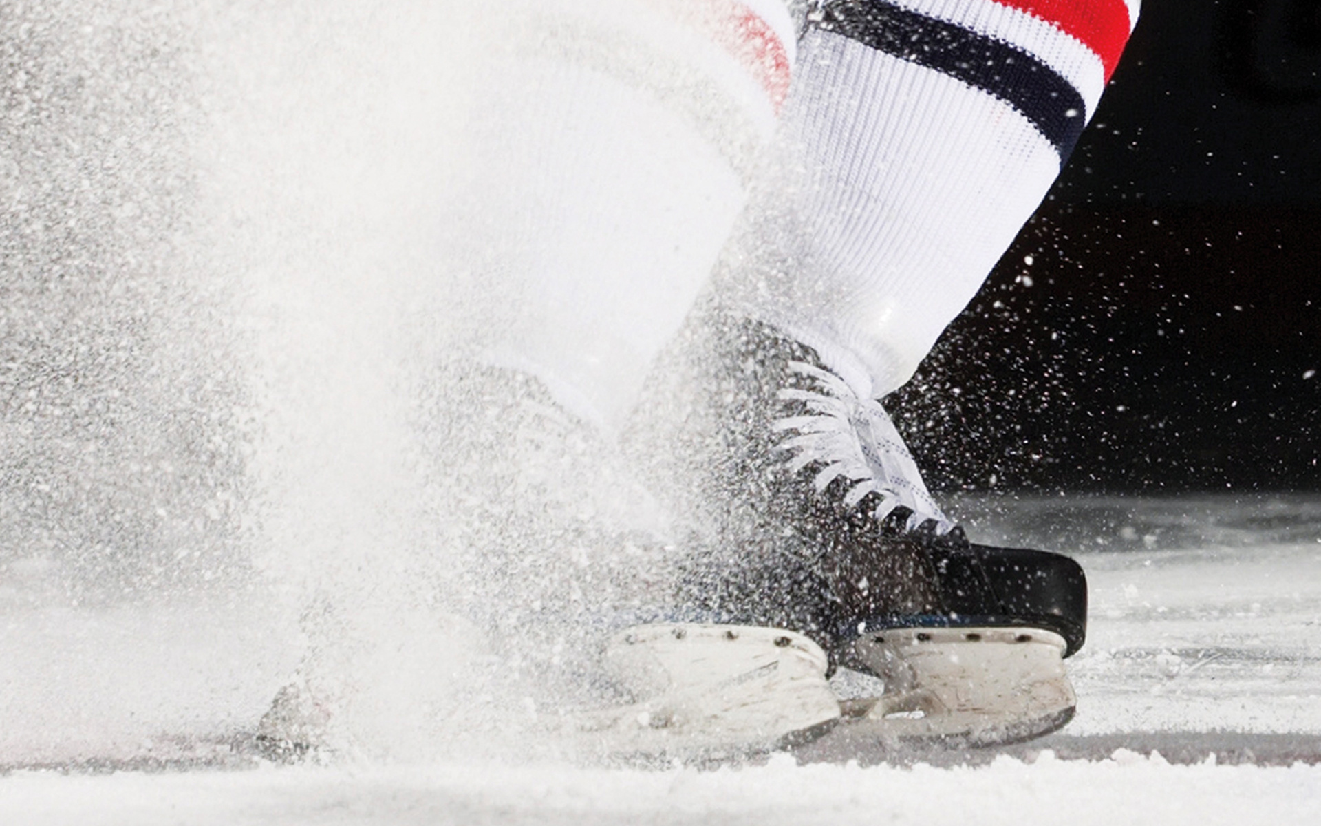 Hockey player's skates spraying ice shavings during an action shot, perfect for hockey wallpapers