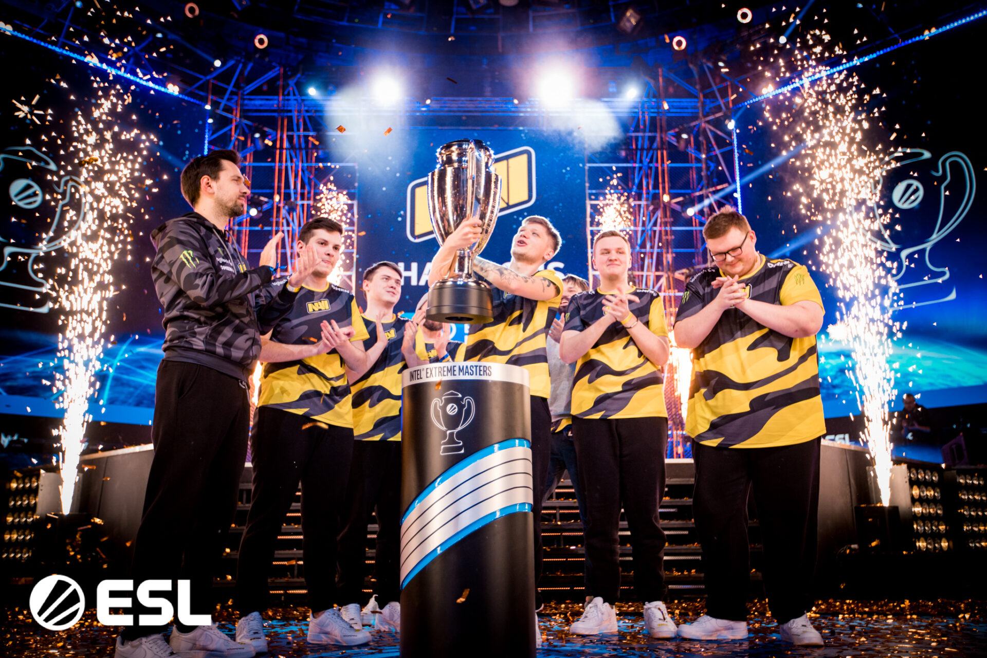 A team celebrating their victory at an Intel Extreme Masters tournament, holding the trophy and surrounded by sparklers and confetti