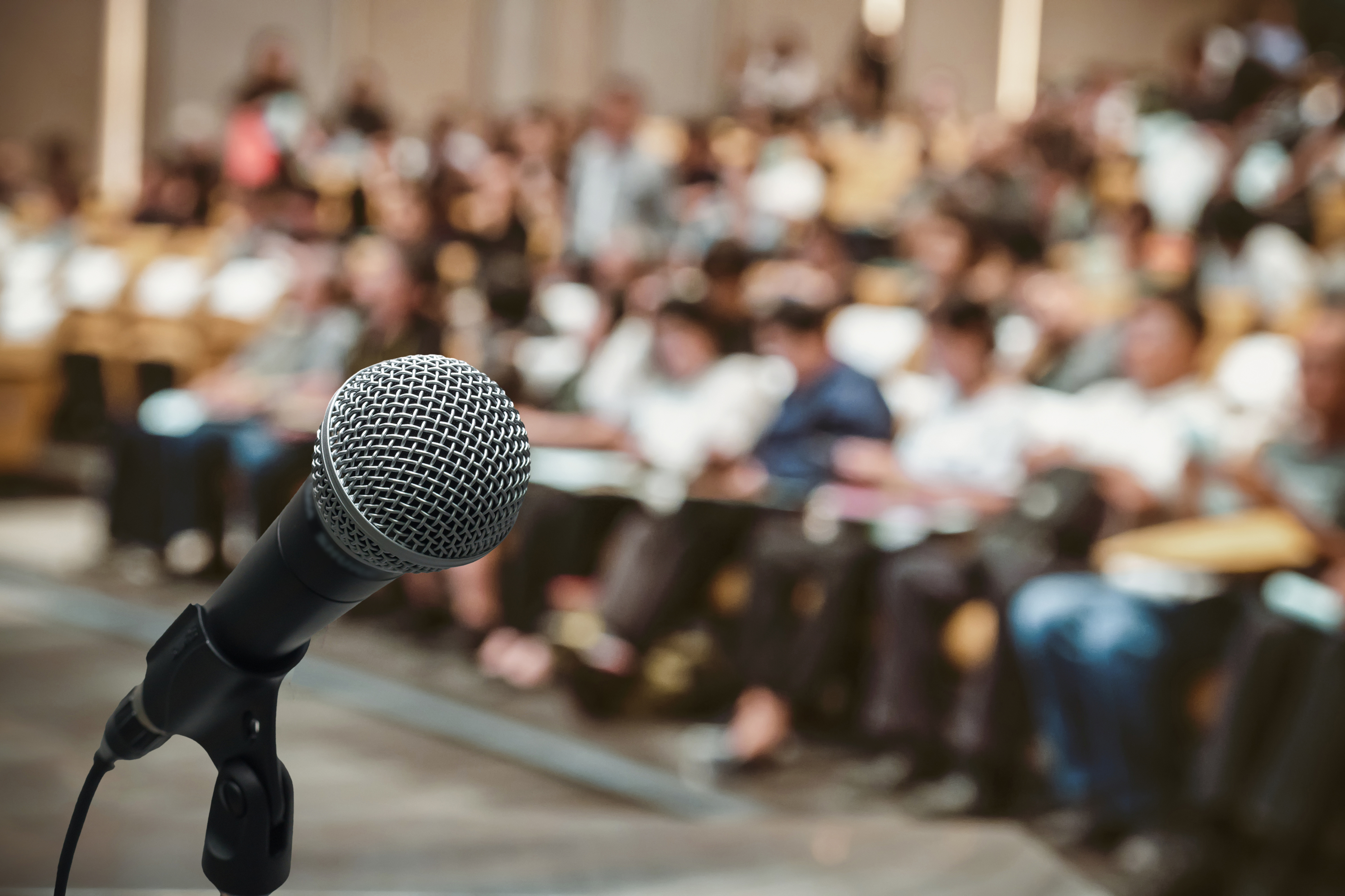 Microphone Over The Abstract Blurred Photo Of Conference Hall Or