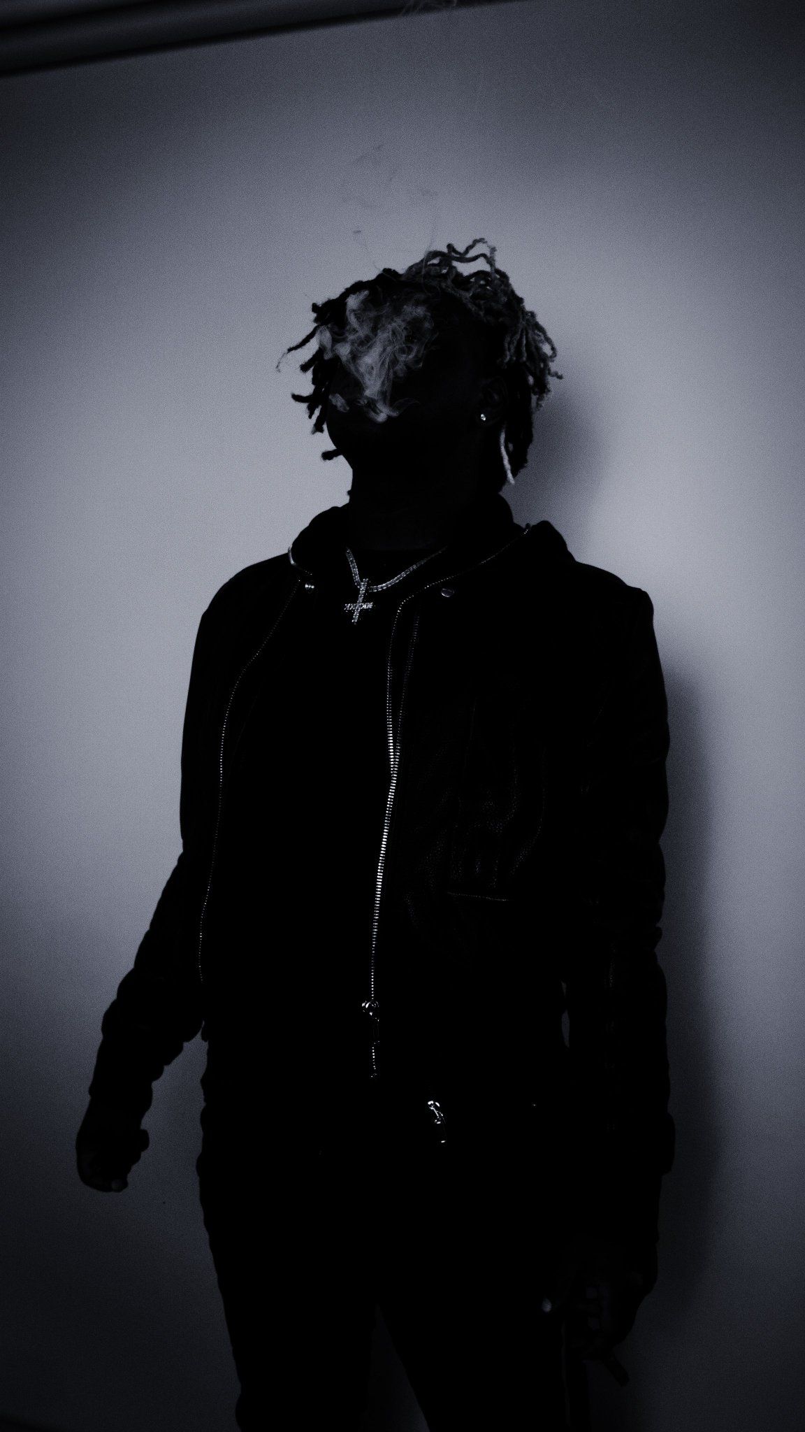 Ken Carson in silhouette, wearing a black jacket and a cross necklace, with smoke around his face