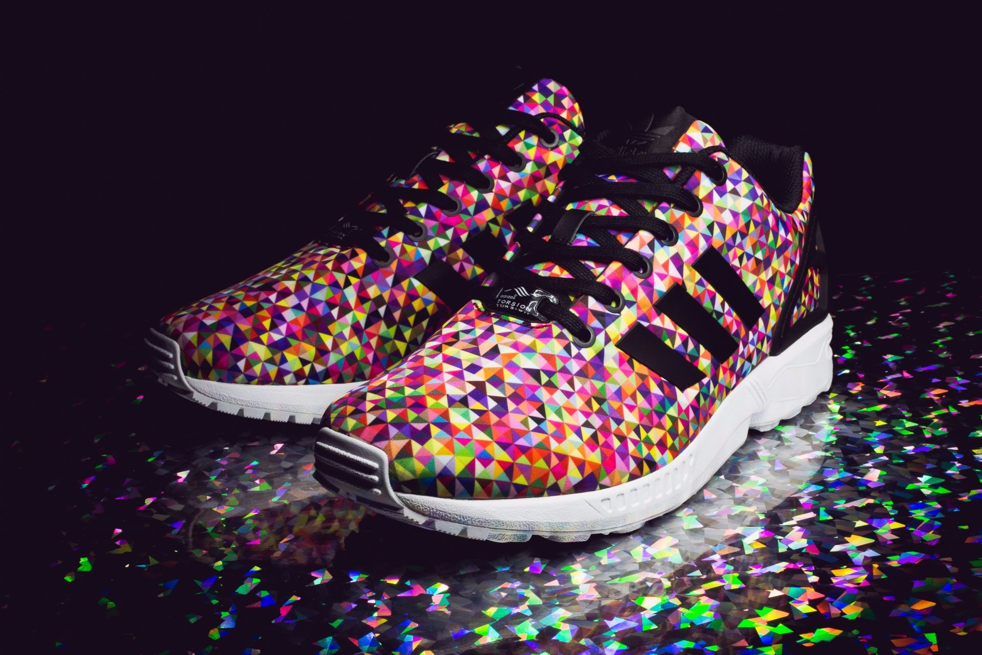Close-up of Adidas ZX Flux sneakers with a colorful geometric pattern on a sparkly surface