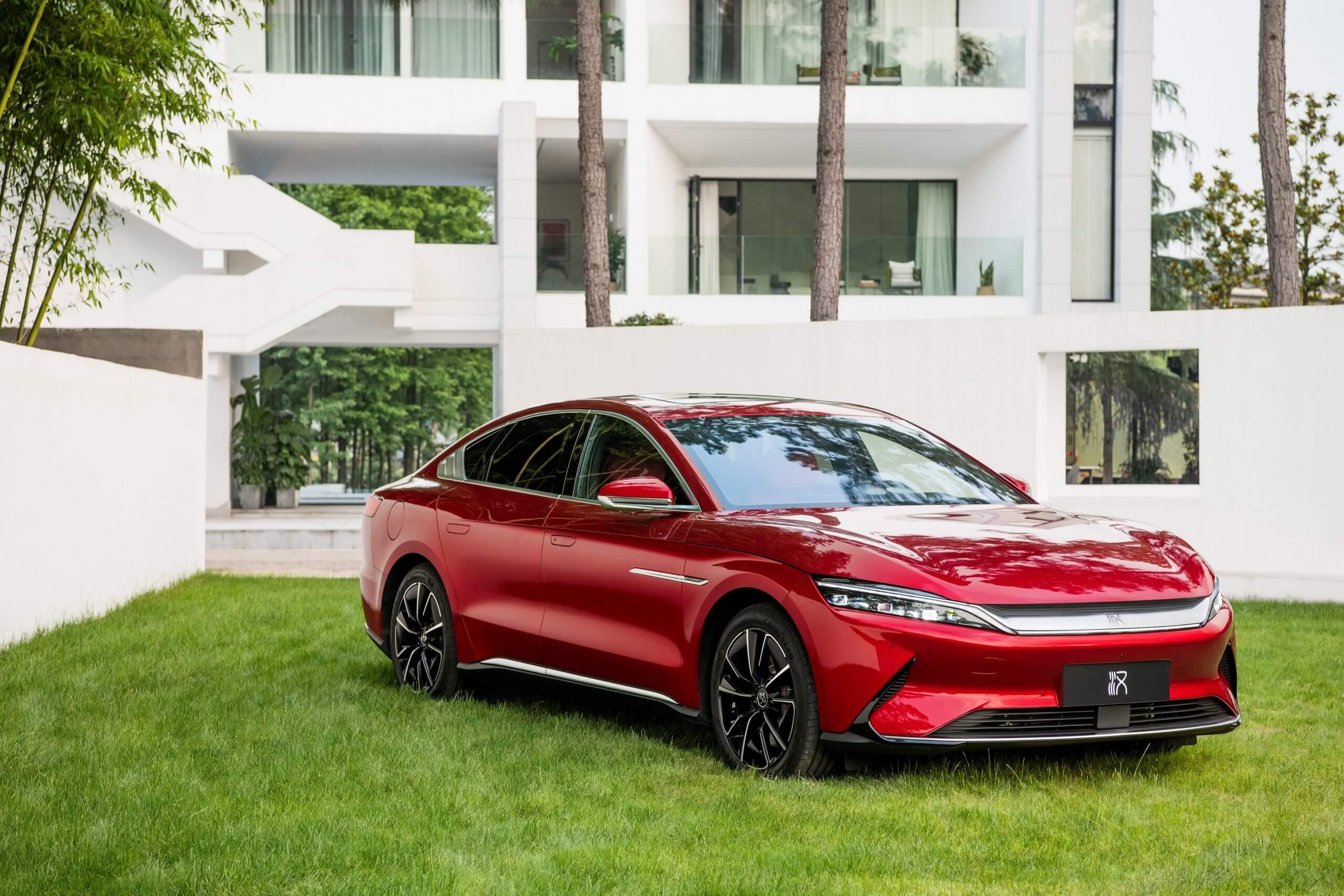 A vibrant red BYD Seal electric sedan parked on a lush green lawn in front of a modern white building