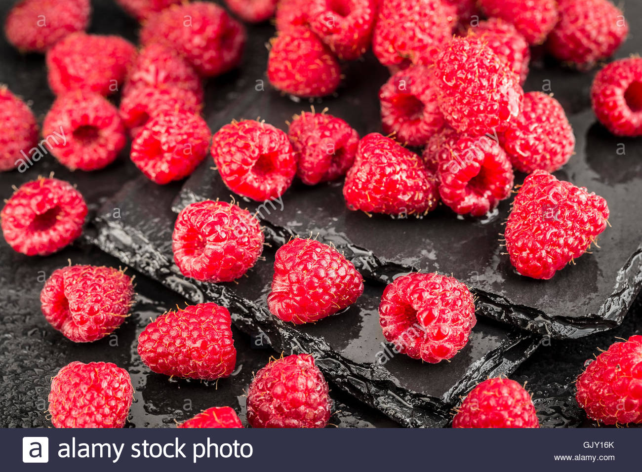 Wet Red Raspberries On A Black Slate Background Stock Photo
