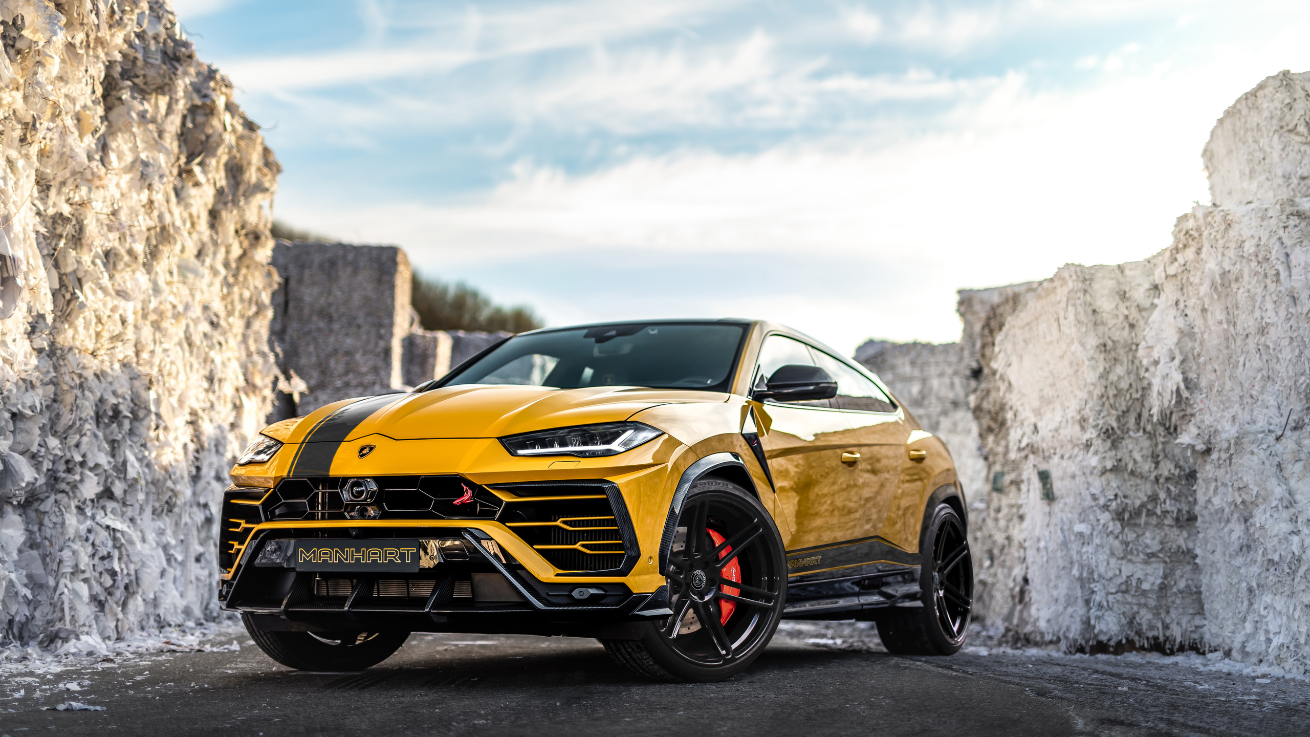A modified yellow Lamborghini Urus by Manhart Performance, parked between large stacks of white material