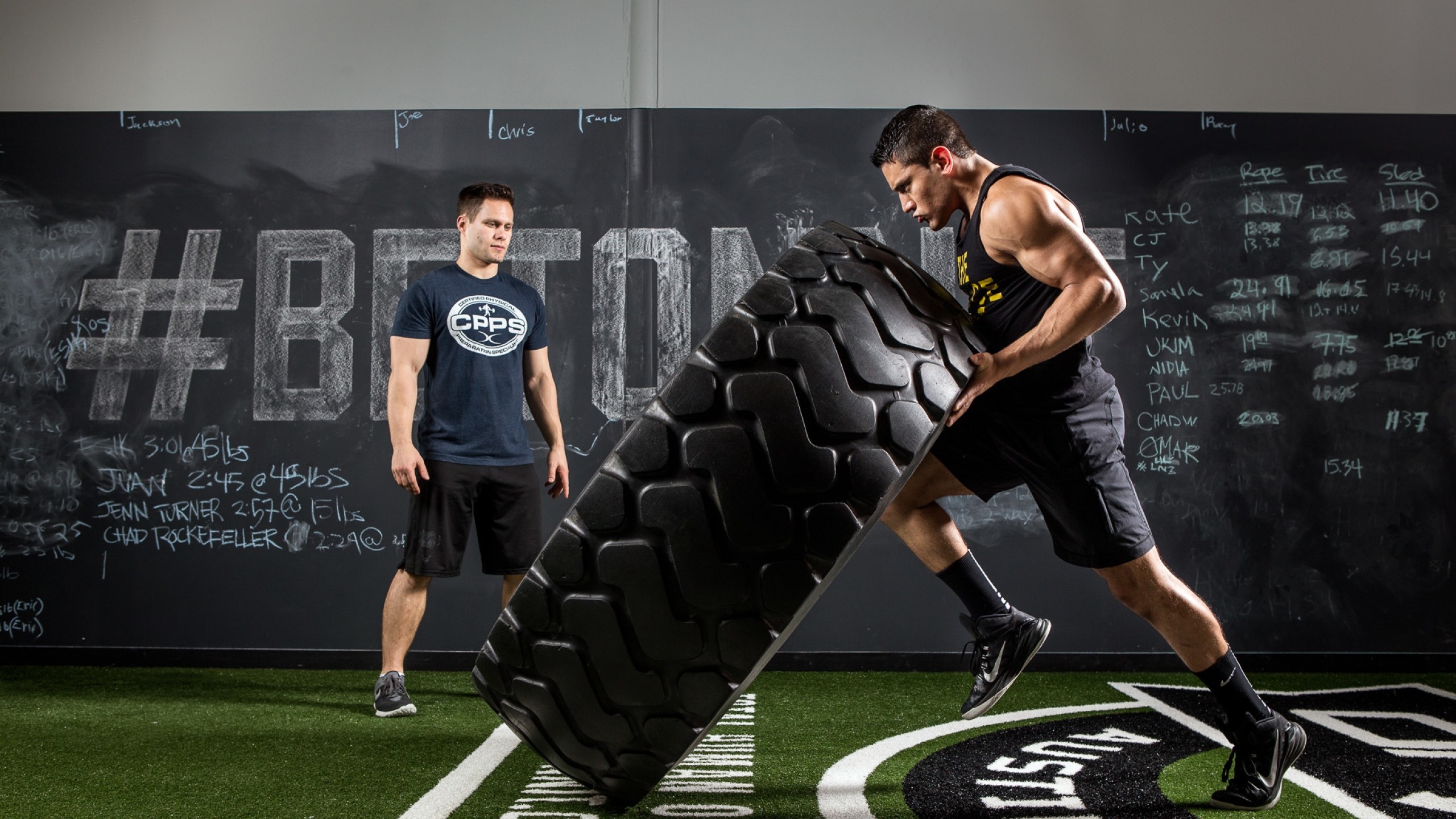 A CrossFit athlete flips a large tire in a gym, demonstrating strength and conditioning training