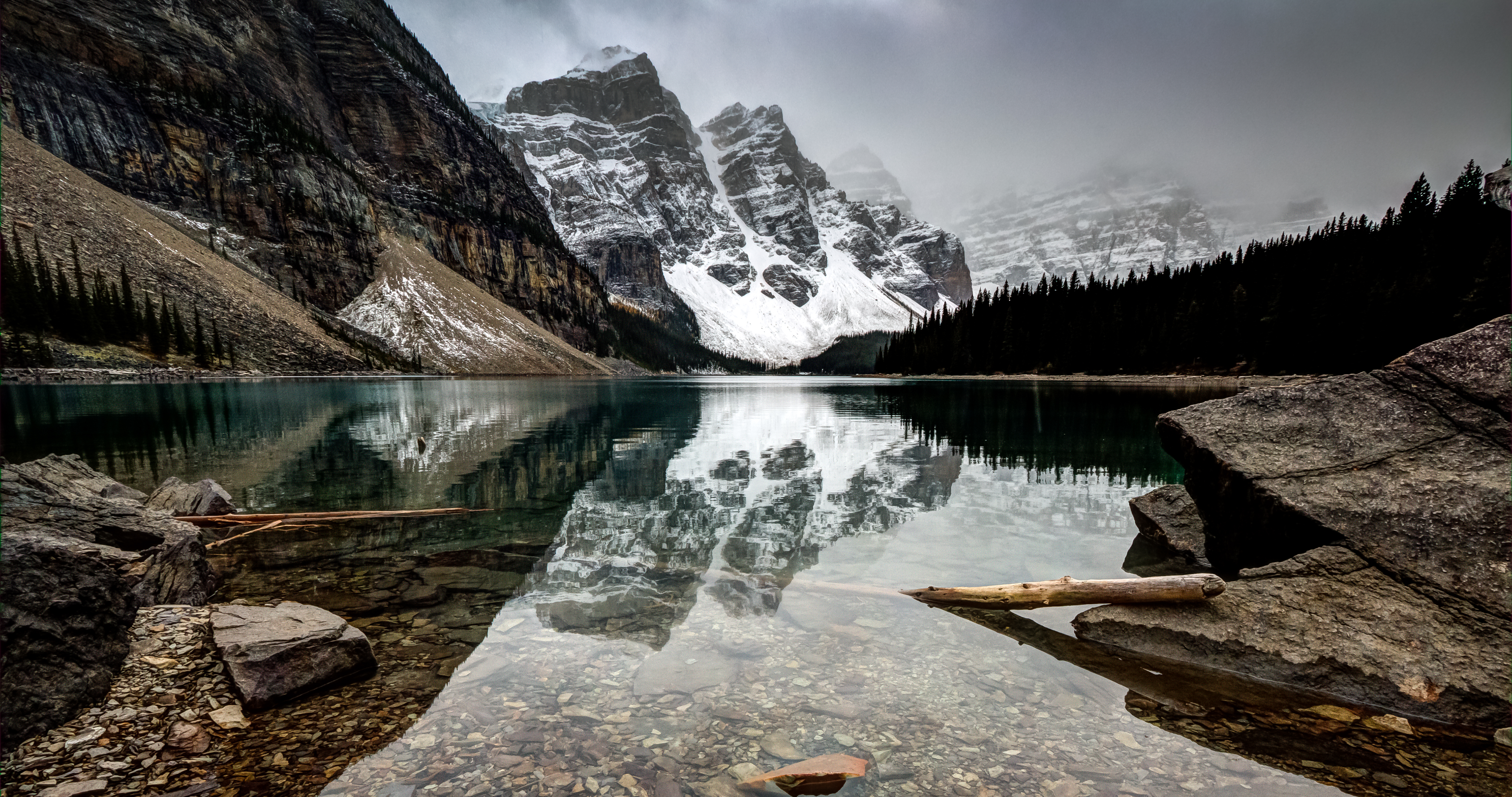 Stunning 4K background image of a pristine lake reflecting snow-capped mountains and a cloudy sky