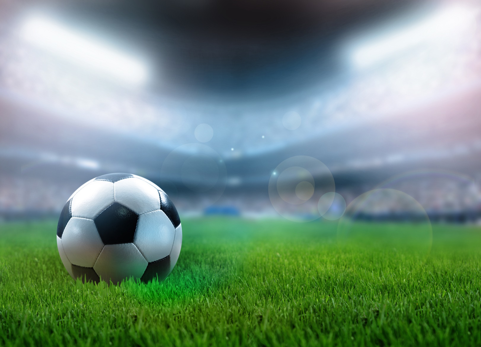 A classic black and white soccer ball sits on a lush green field in a brightly lit stadium, ready for the big game