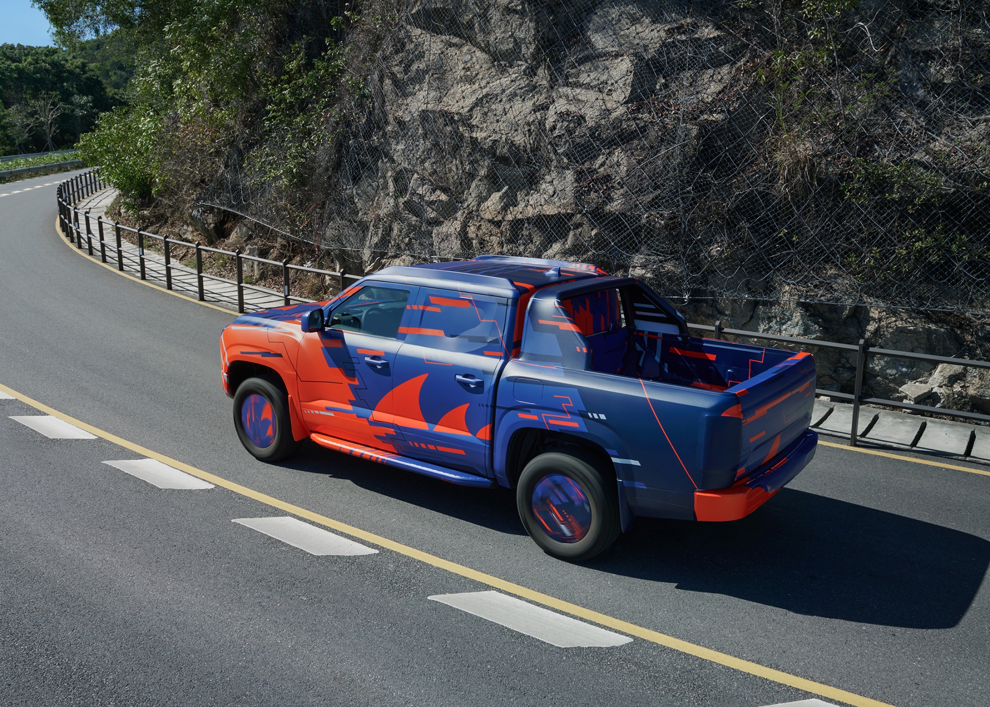 A stylish BYD electric pickup truck, adorned with a vibrant shark-themed design, cruises along a coastal highway