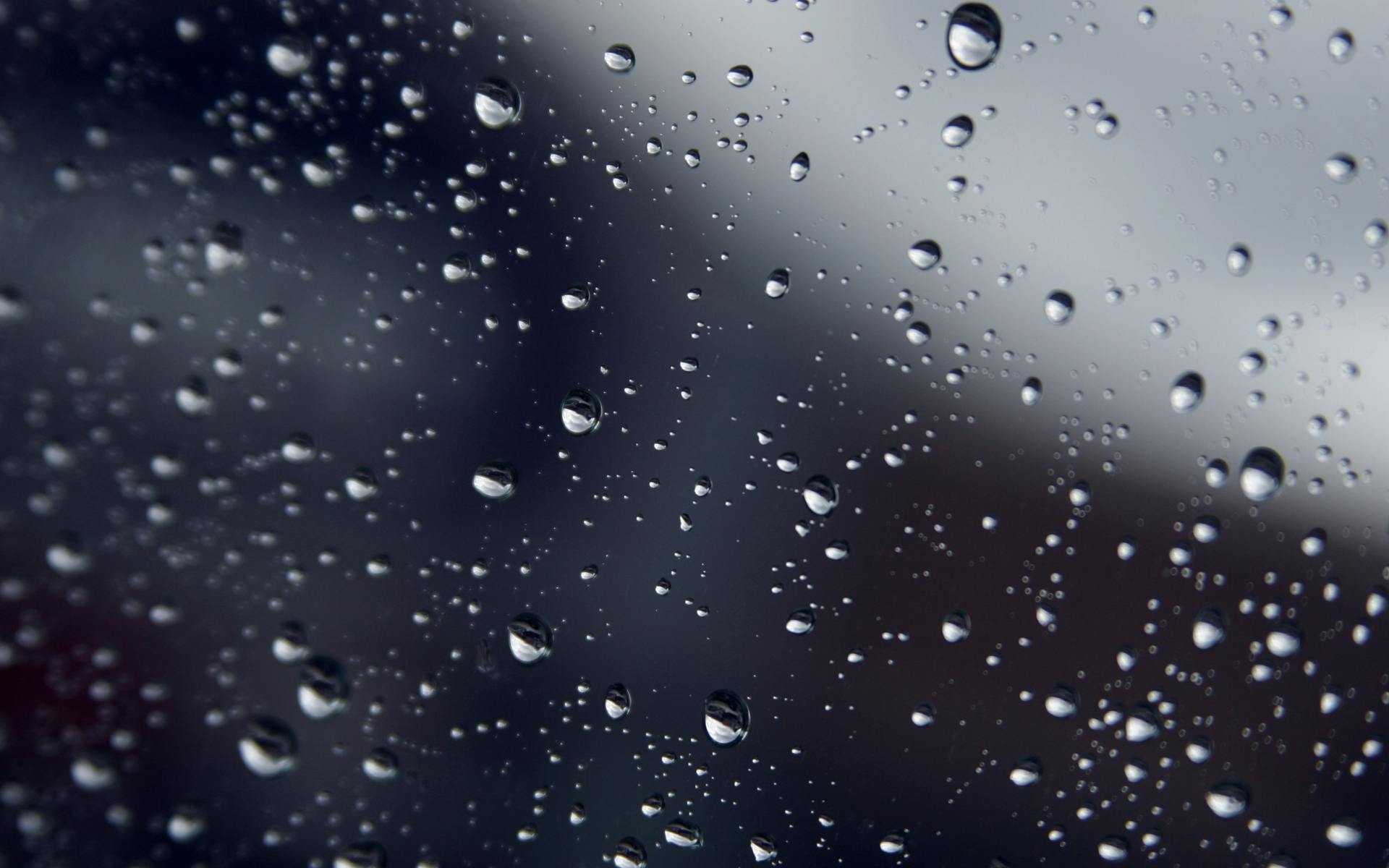Close-up of raindrops clinging to a window pane, with a blurred background