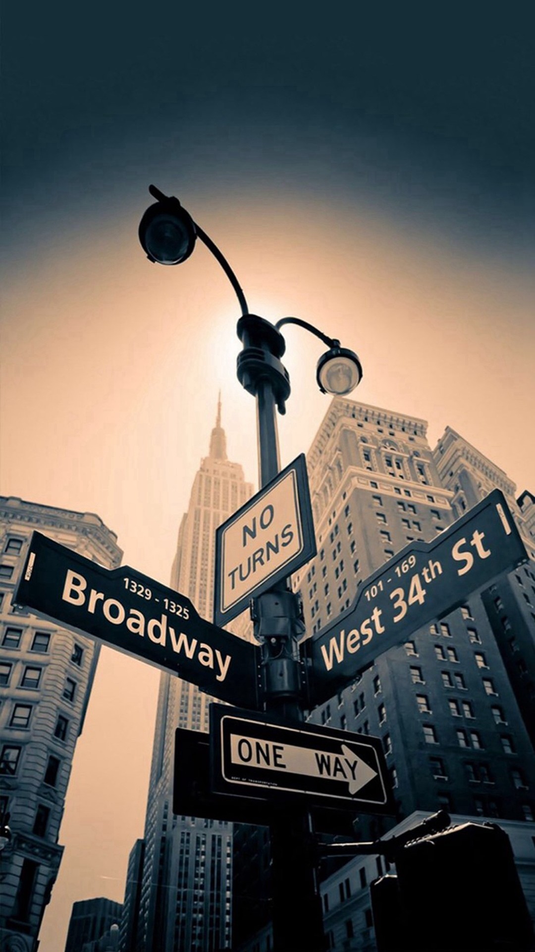A low-angle view of a bustling intersection on Broadway in New York City, showcasing the iconic street signs and a glimpse of the Empire State Building in the background
