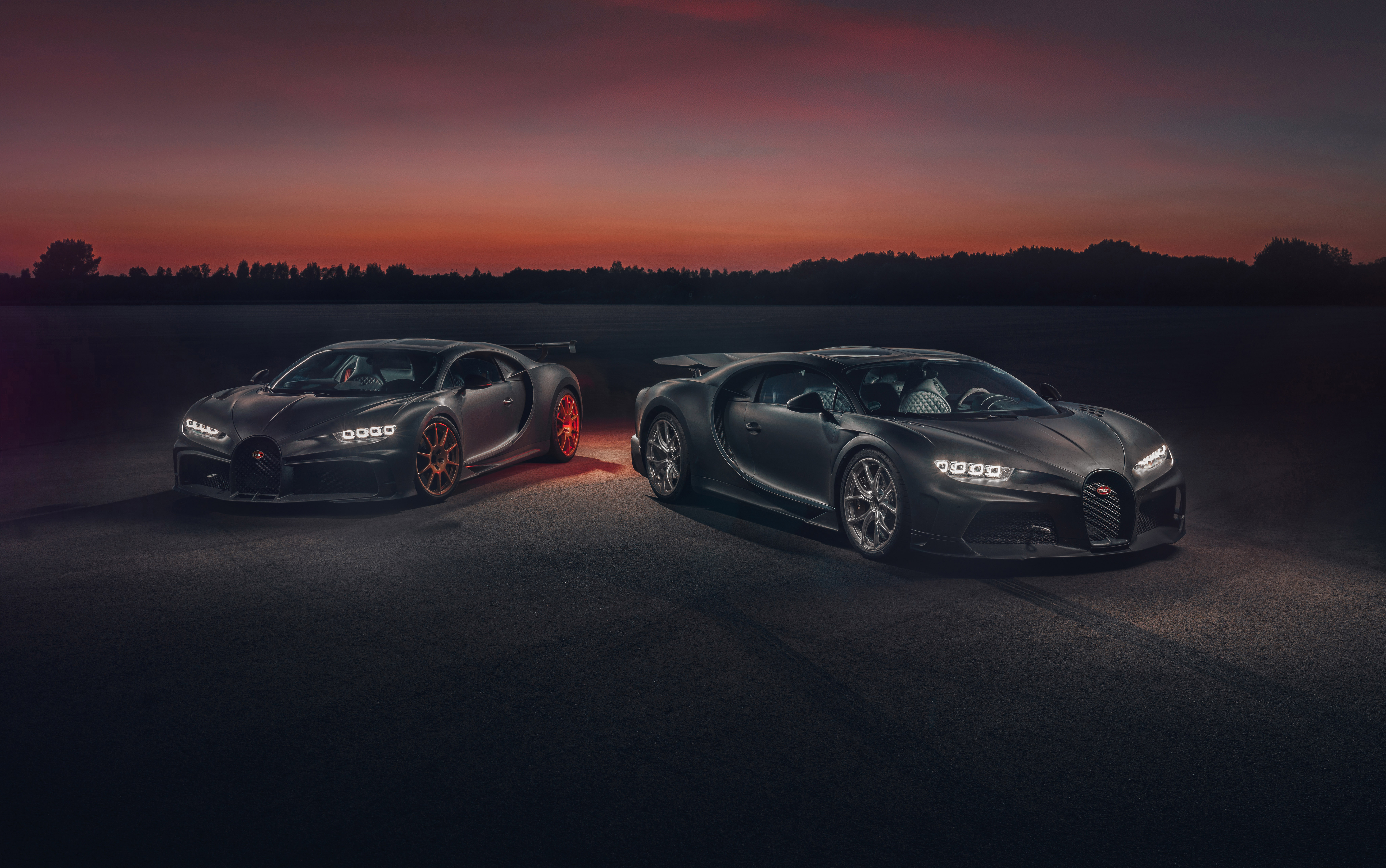Two Bugatti Chiron Super Sport hypercars parked side by side against a dramatic sunset backdrop
