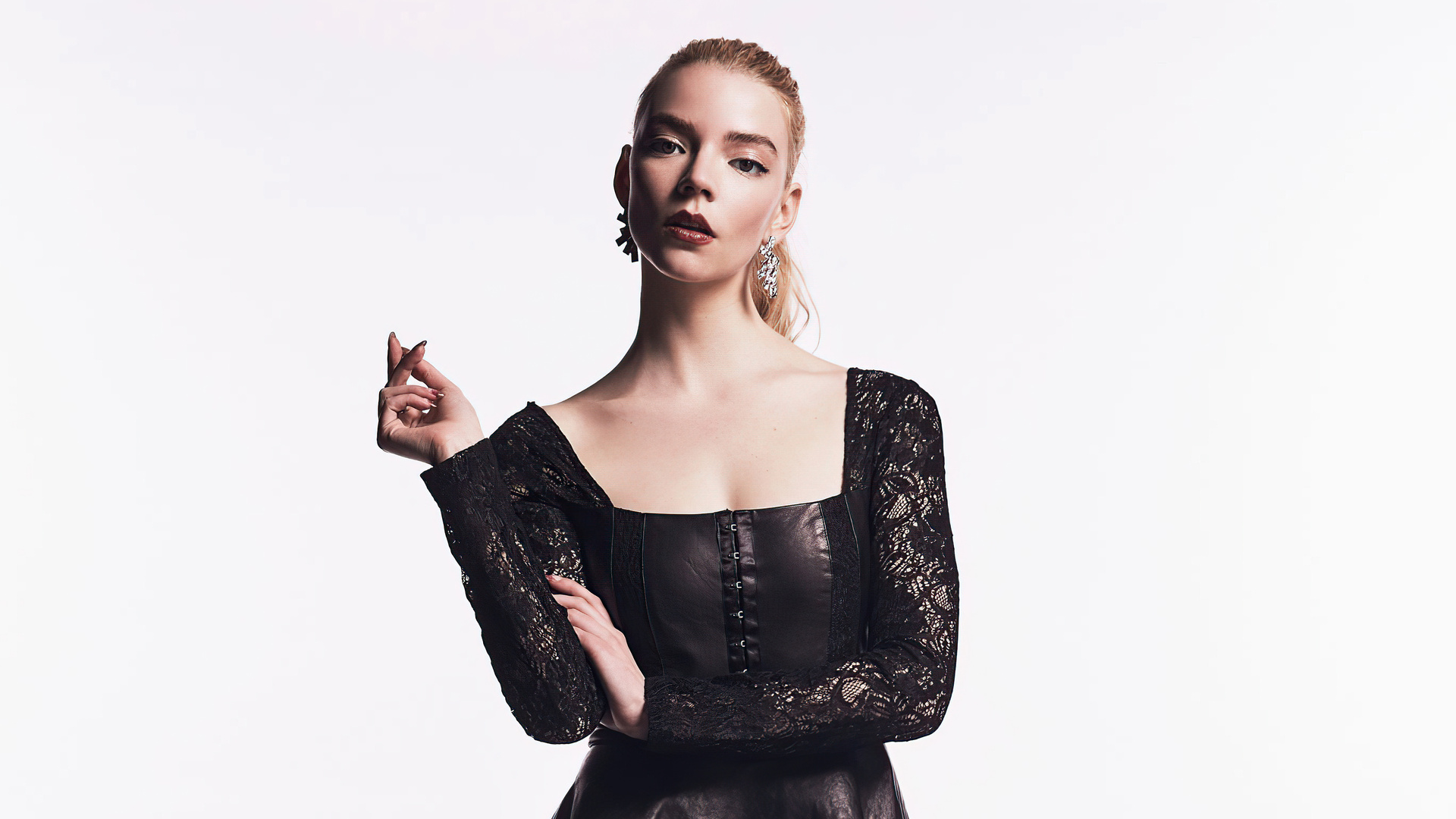 Anya Taylor-Joy posing in a black dress with lace sleeves against a white background