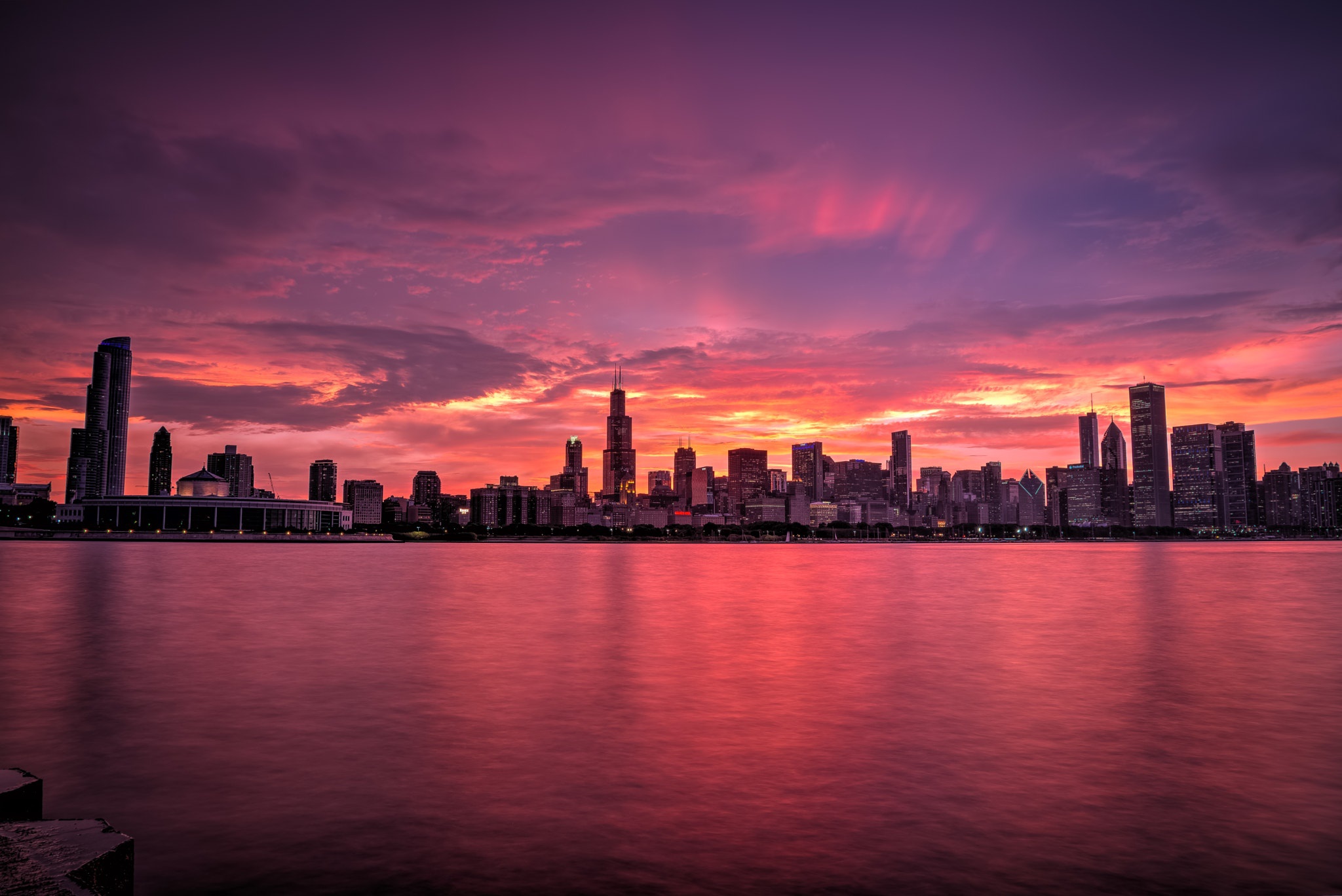Chicago skyline at sunset with vibrant pink and purple sky reflected in the calm waters of Lake Michigan